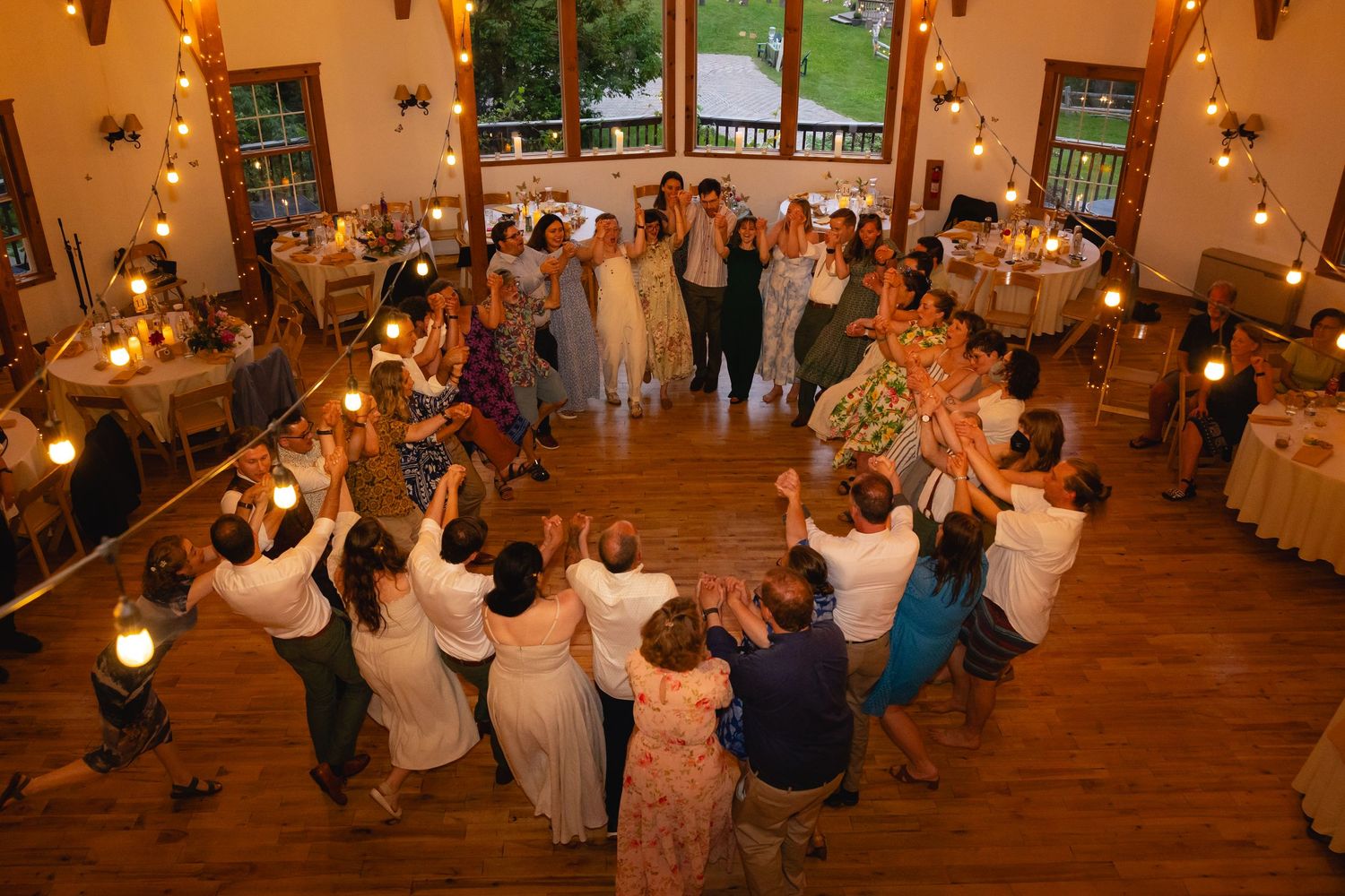 Outdoor wedding ceremony under a wooden gazebo surrounded by trees with guests seated in orange folding chairs.