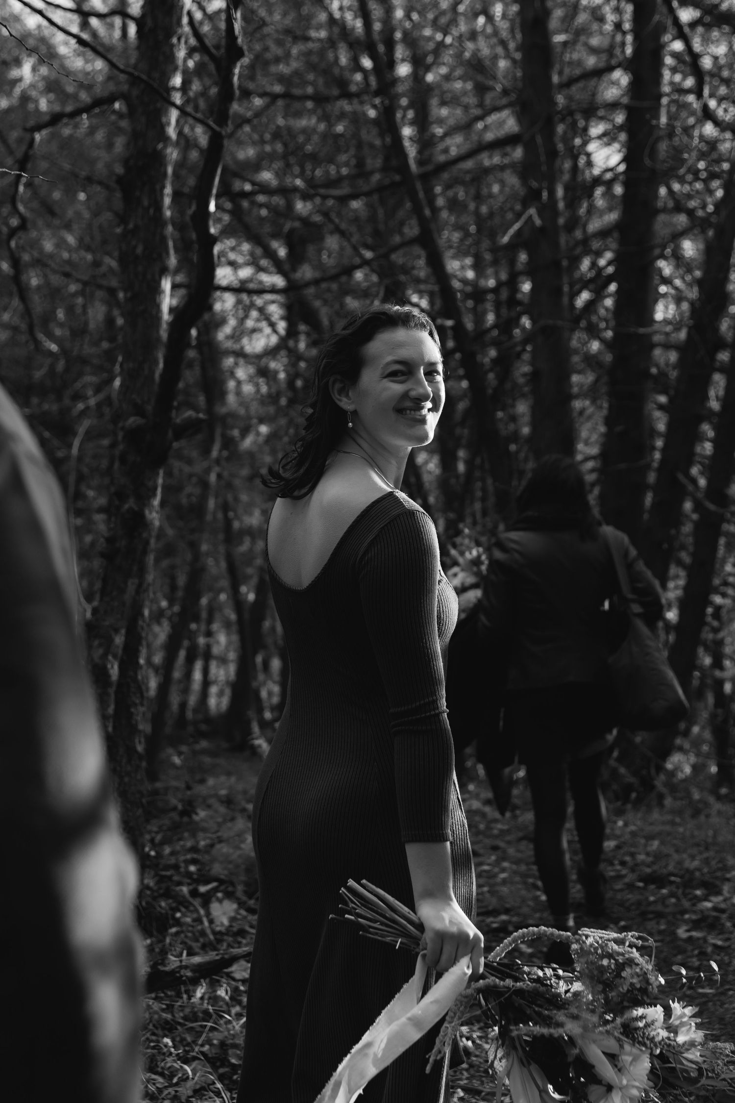A black and white photo of someone in an elegant black dress standing in a moody forest setting.