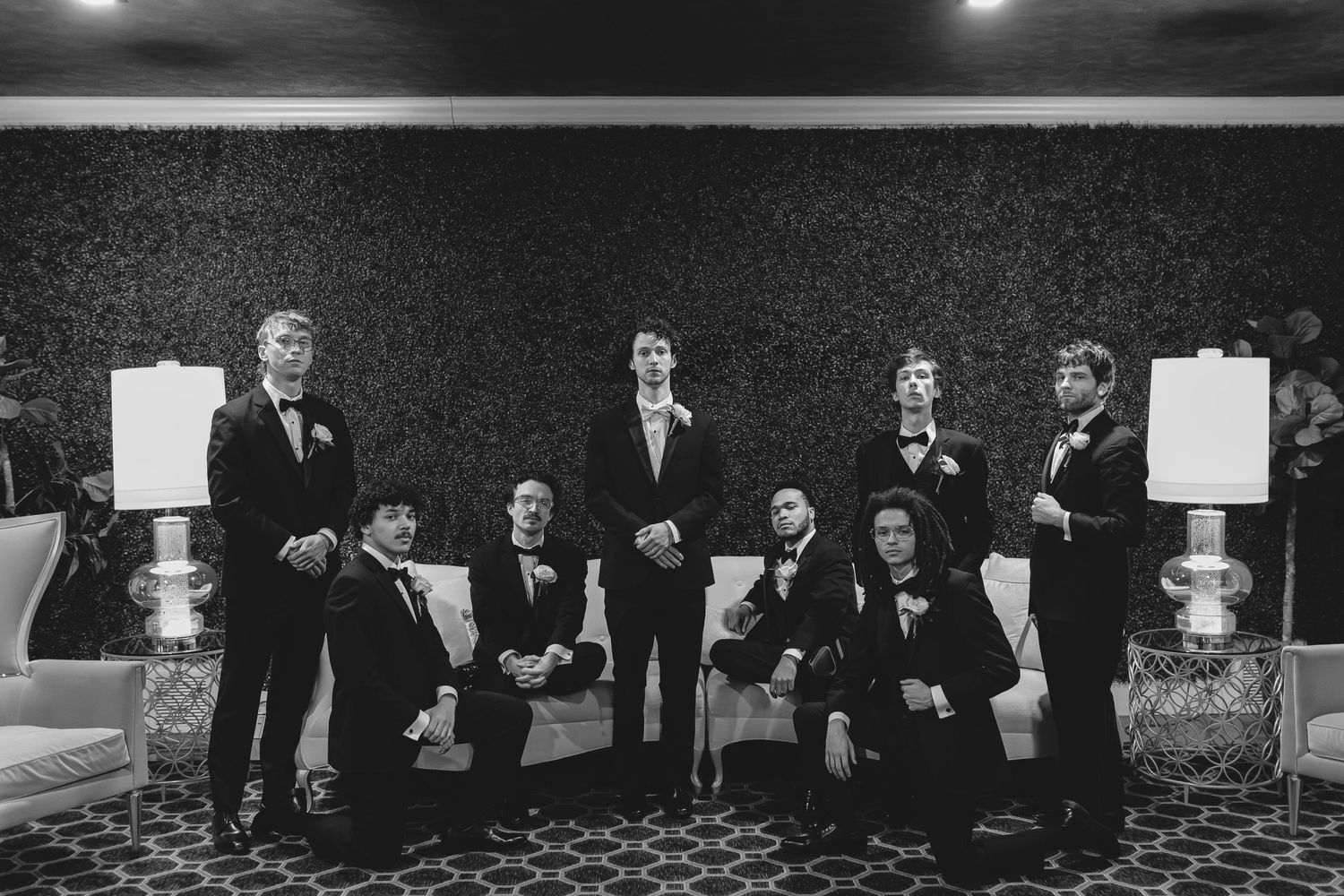Wedding party in formal attire poses together in elegant monochrome setting with decorative table lamps.