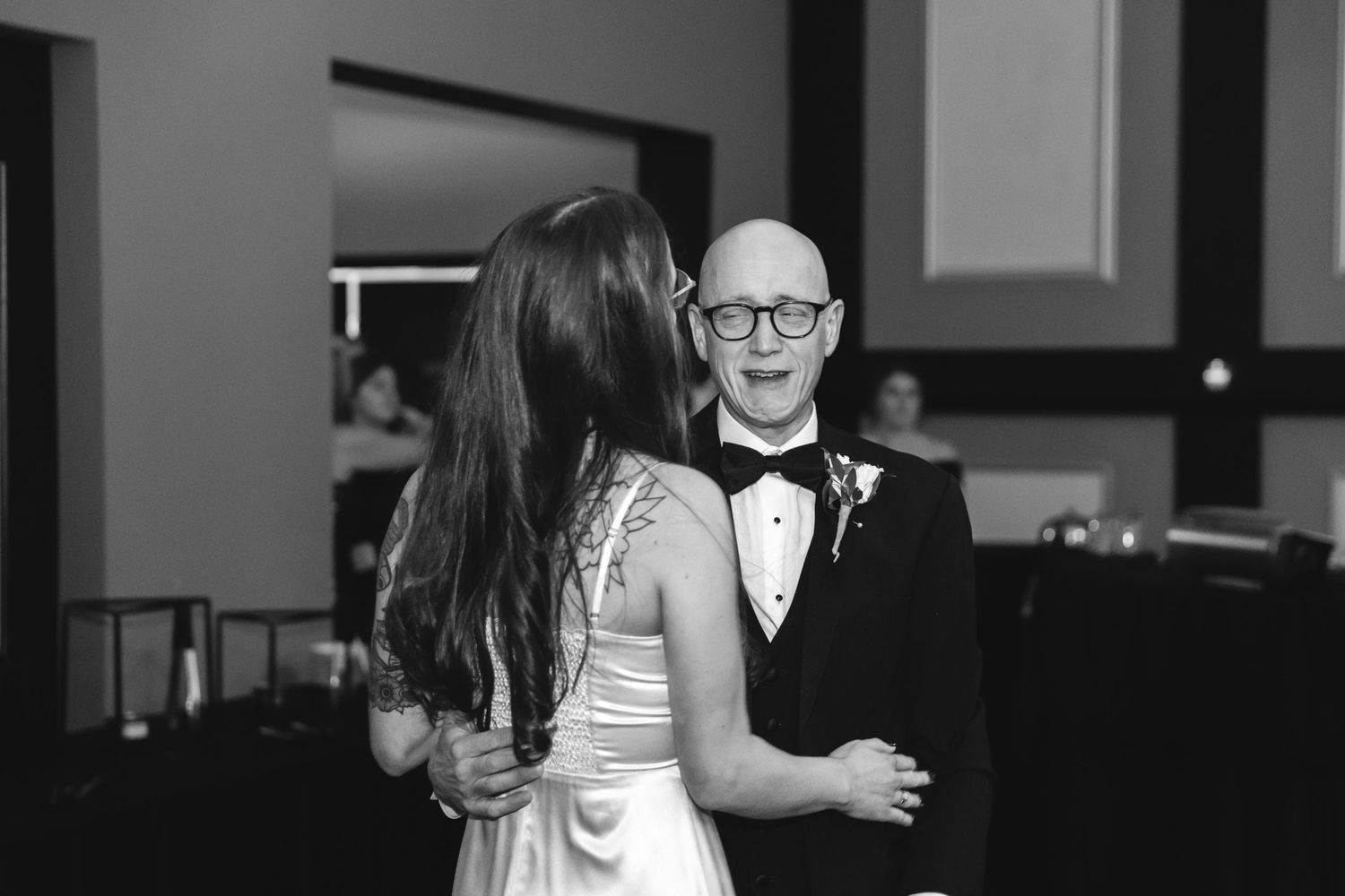 A black and white photo of a couple dancing together at a formal event, with the partner wearing a tuxedo and bow tie.