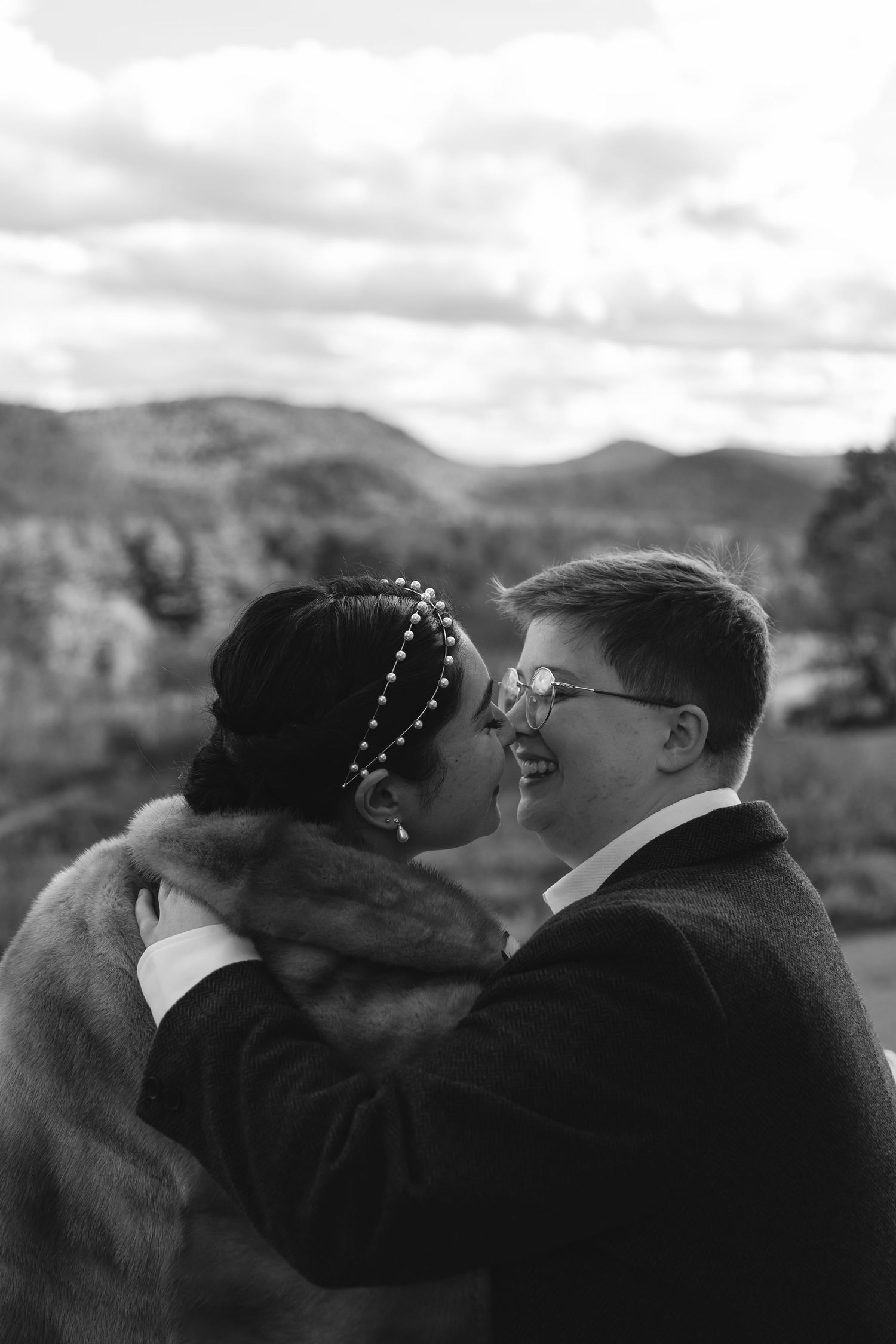 An intimate black and white portrait of a couple embracing against a mountain backdrop.