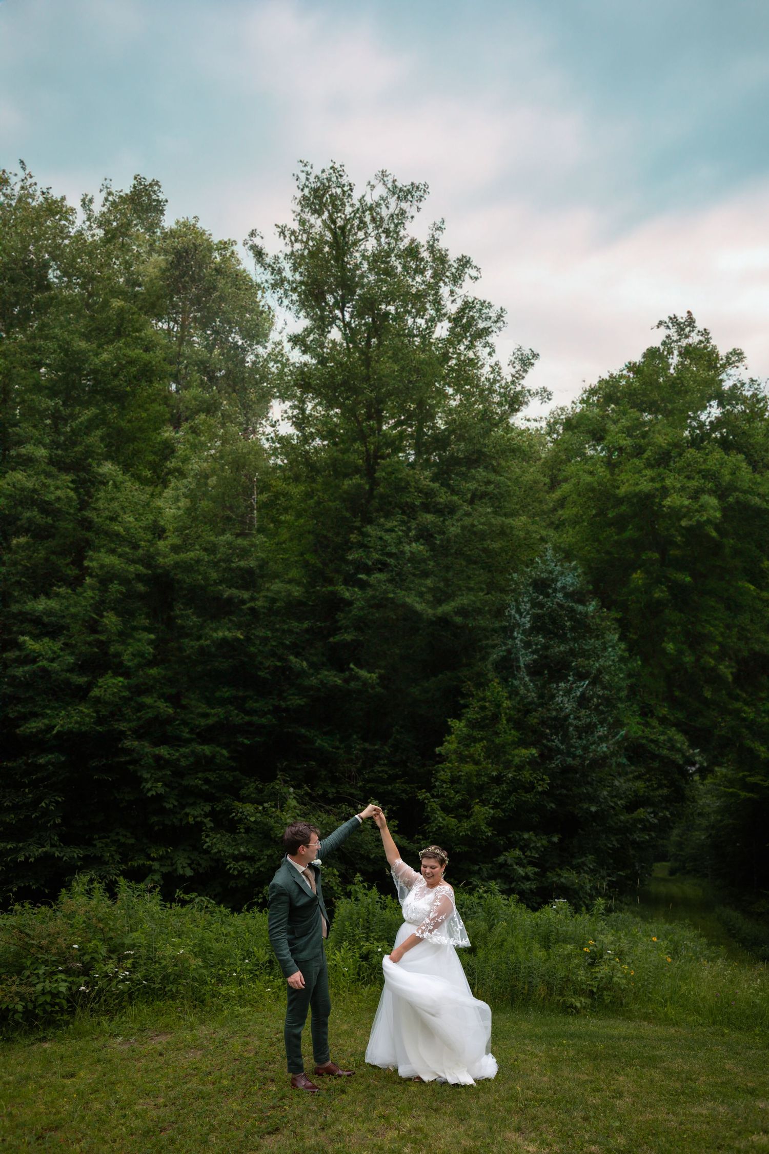 A couple dancing on a grassy lawn surrounded by tall green trees during their wedding celebration.