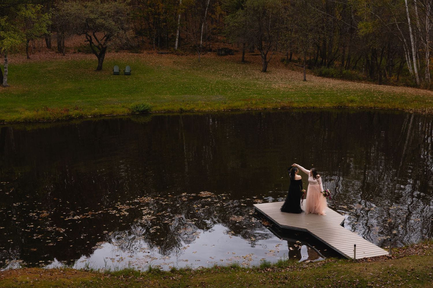 A couple dances on a floating dock over a calm pond surrounded by autumn foliage.