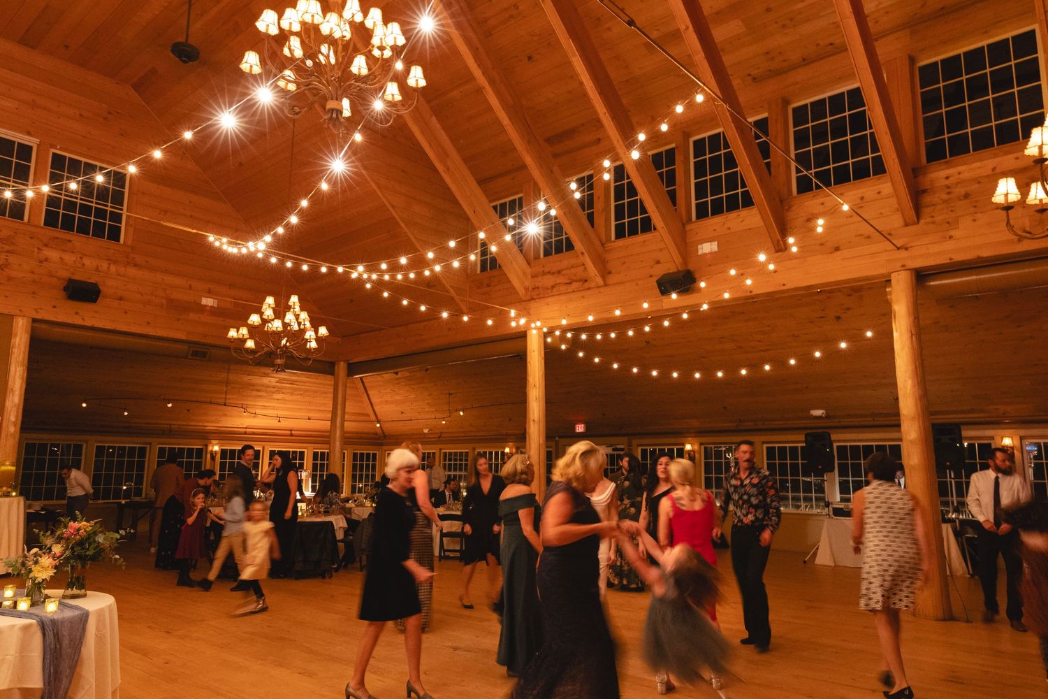 Wedding reception in a wooden barn venue with string lights and chandeliers.