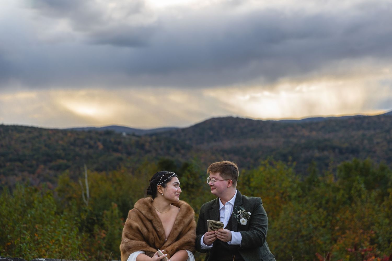 Wedding couple sharing intimate moment on mountaintop with dramatic cloudy sky.