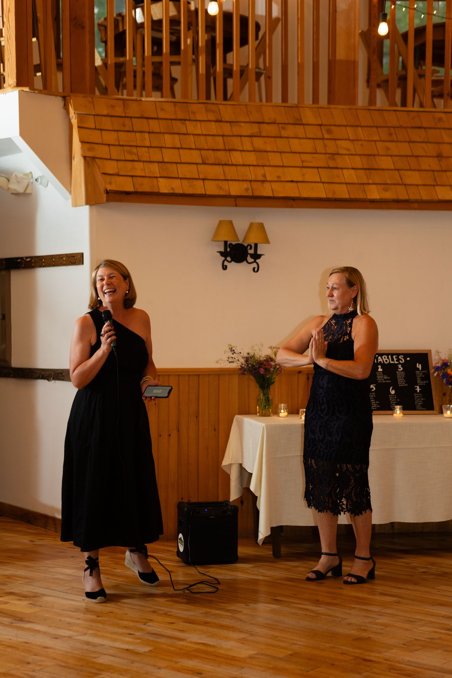 Two performers in black dresses singing on wooden floor at wedding reception.