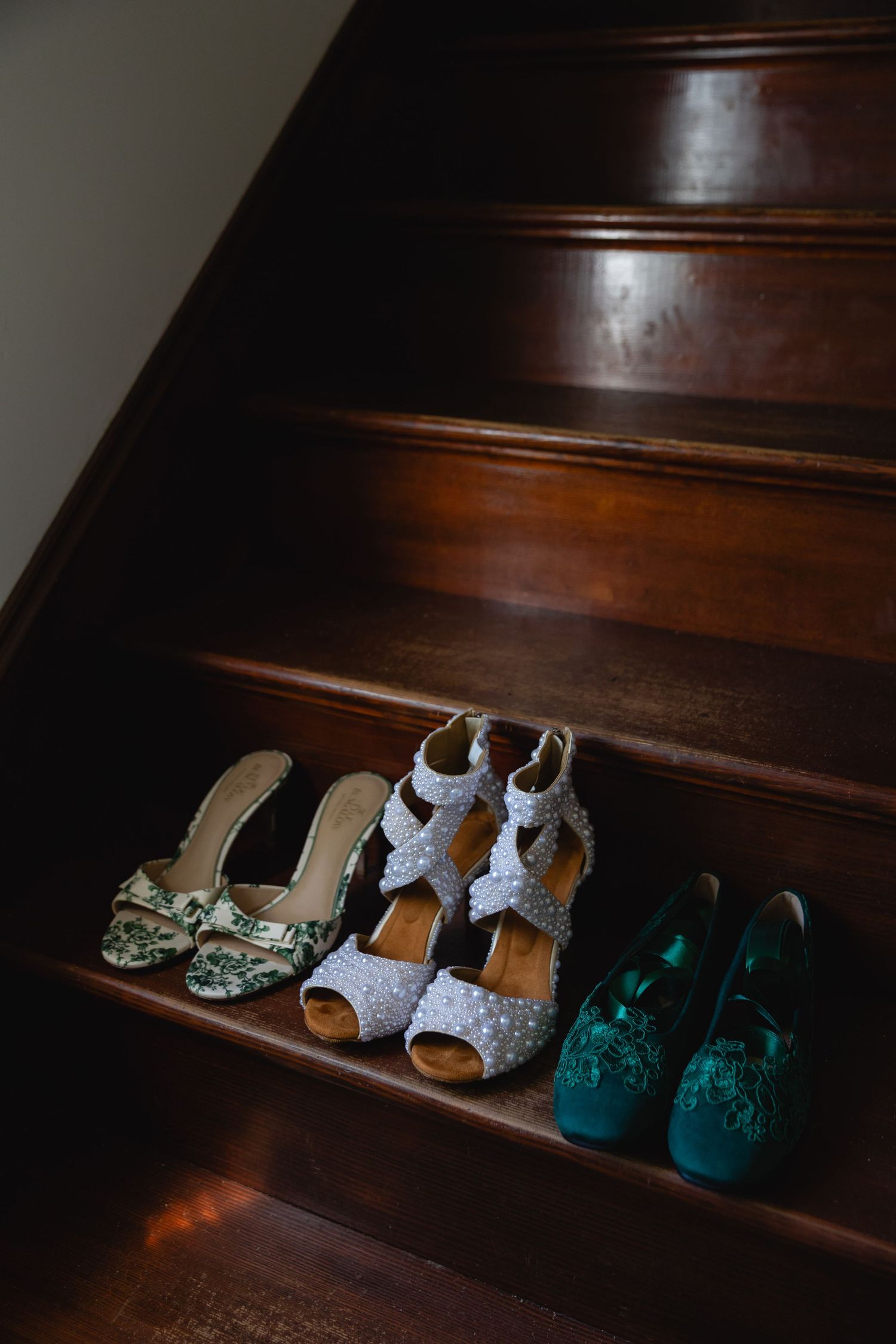 A sequence of small baby shoes lined up on dark wooden stairs, showing a progression of different styles and colors.