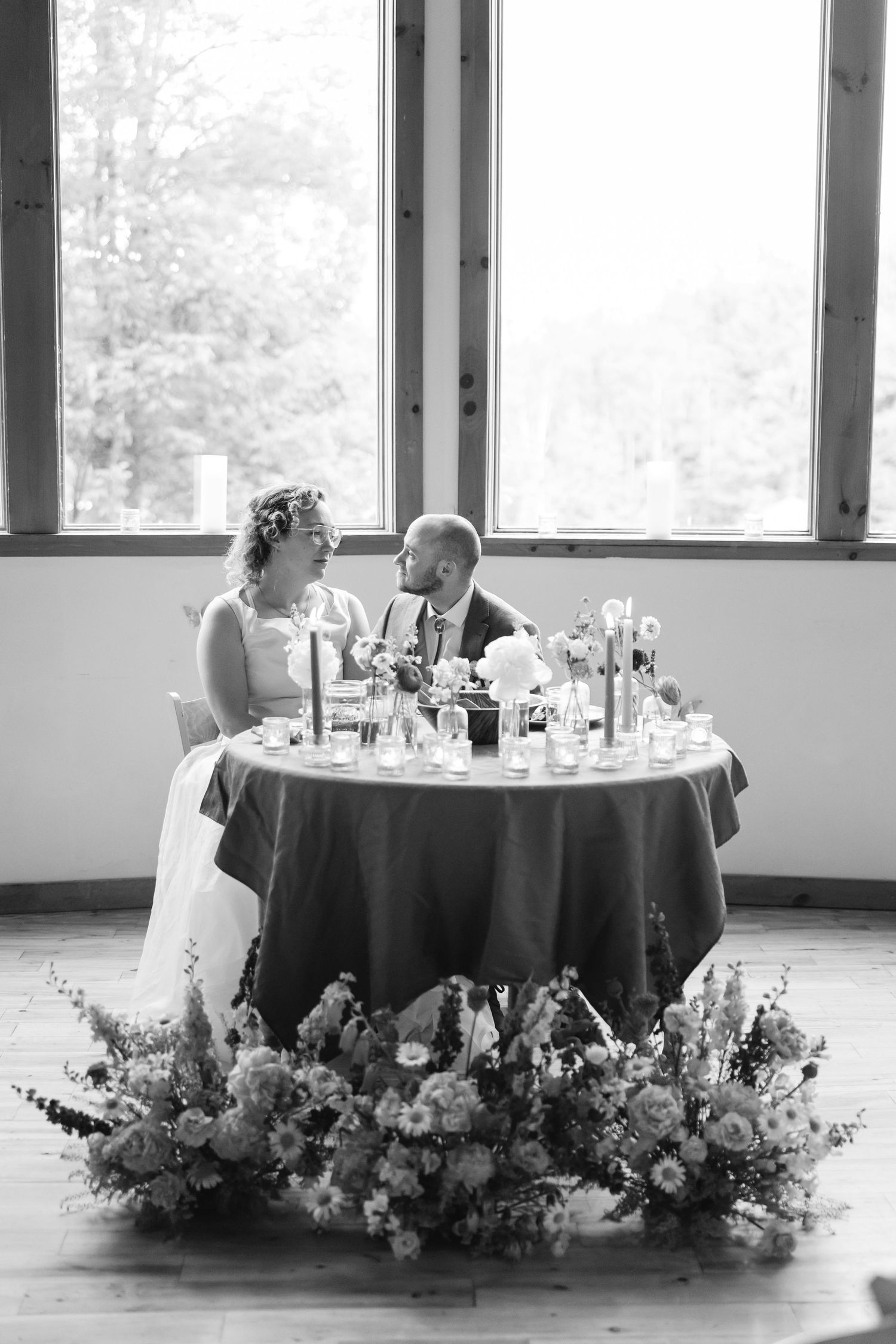 Black and white photo of elegant round reception tables adorned with flowing floral arrangements and place settings.