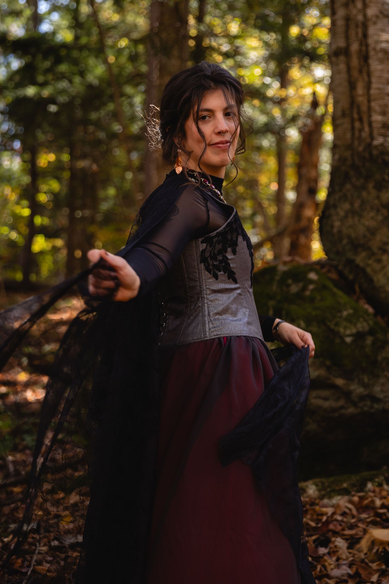 A person in a dark dress and sheer sleeves twirls gracefully among autumn trees in a forest setting.