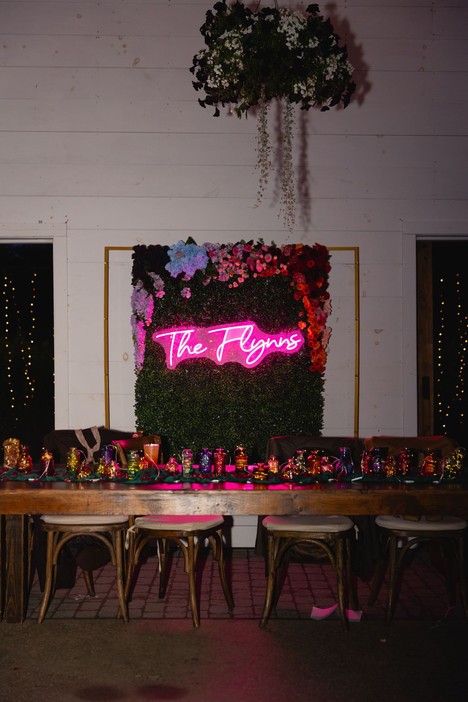 Wedding reception venue decorated with wooden tables, greenery wall backdrop, and glowing pink neon sign creates romantic ambiance.