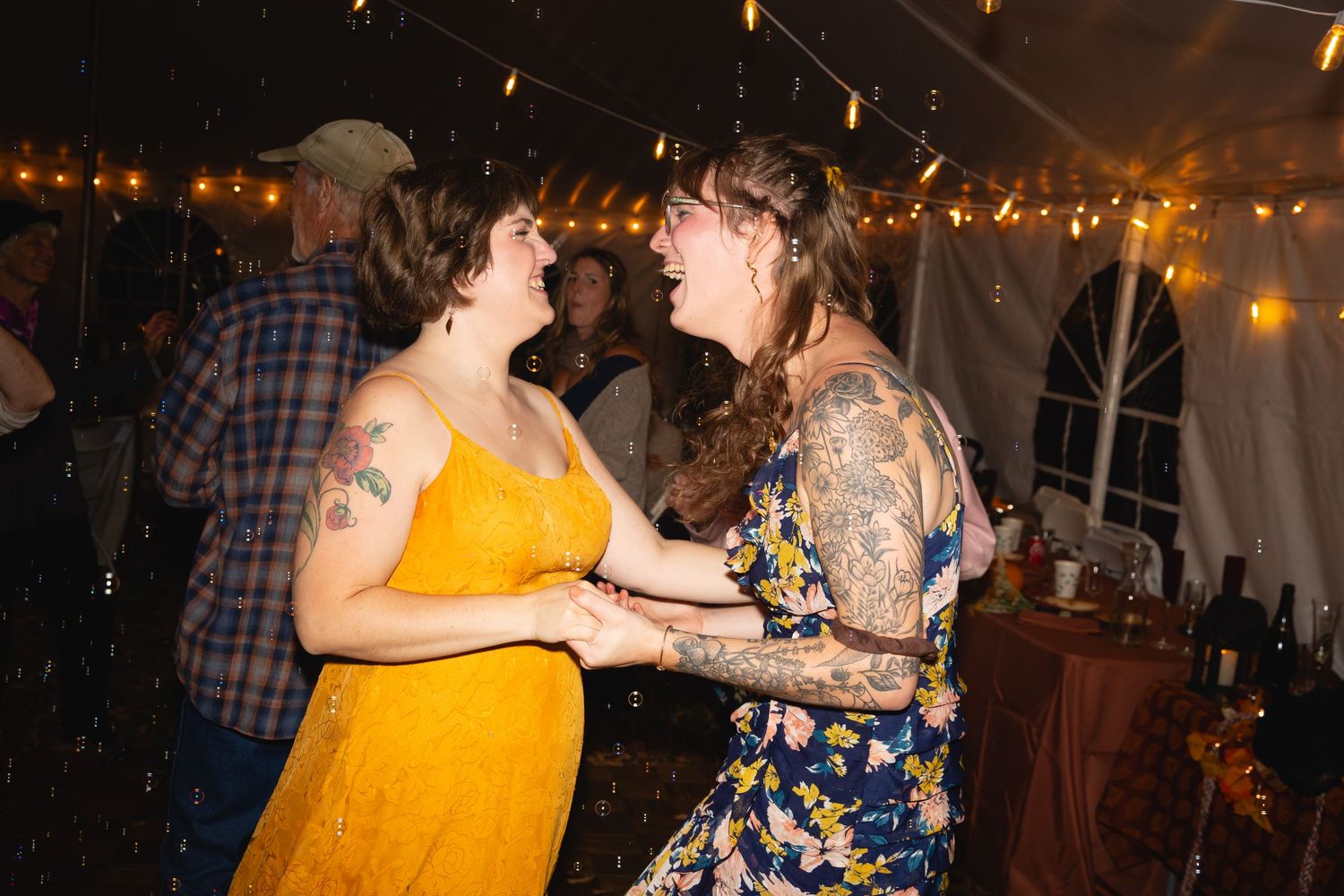 People dancing and celebrating at a dimly lit indoor party venue decorated with string lights.