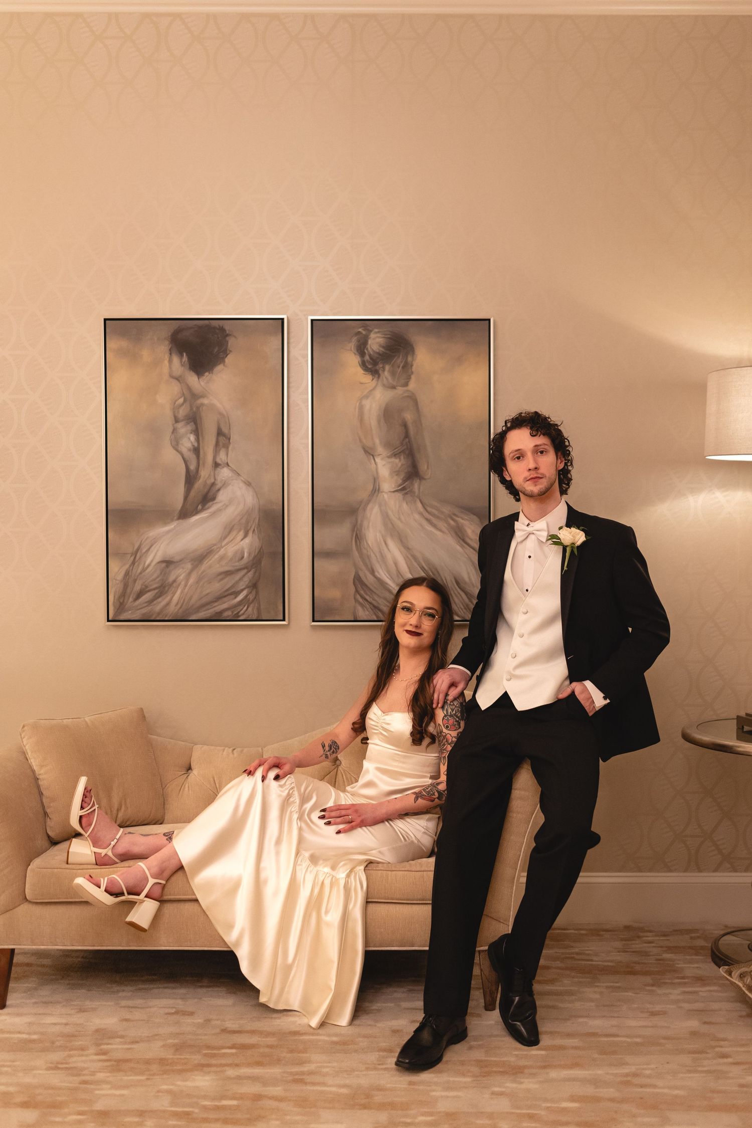 Elegant couple poses in formal attire in a softly lit room with vintage ballerina artwork on the wall.