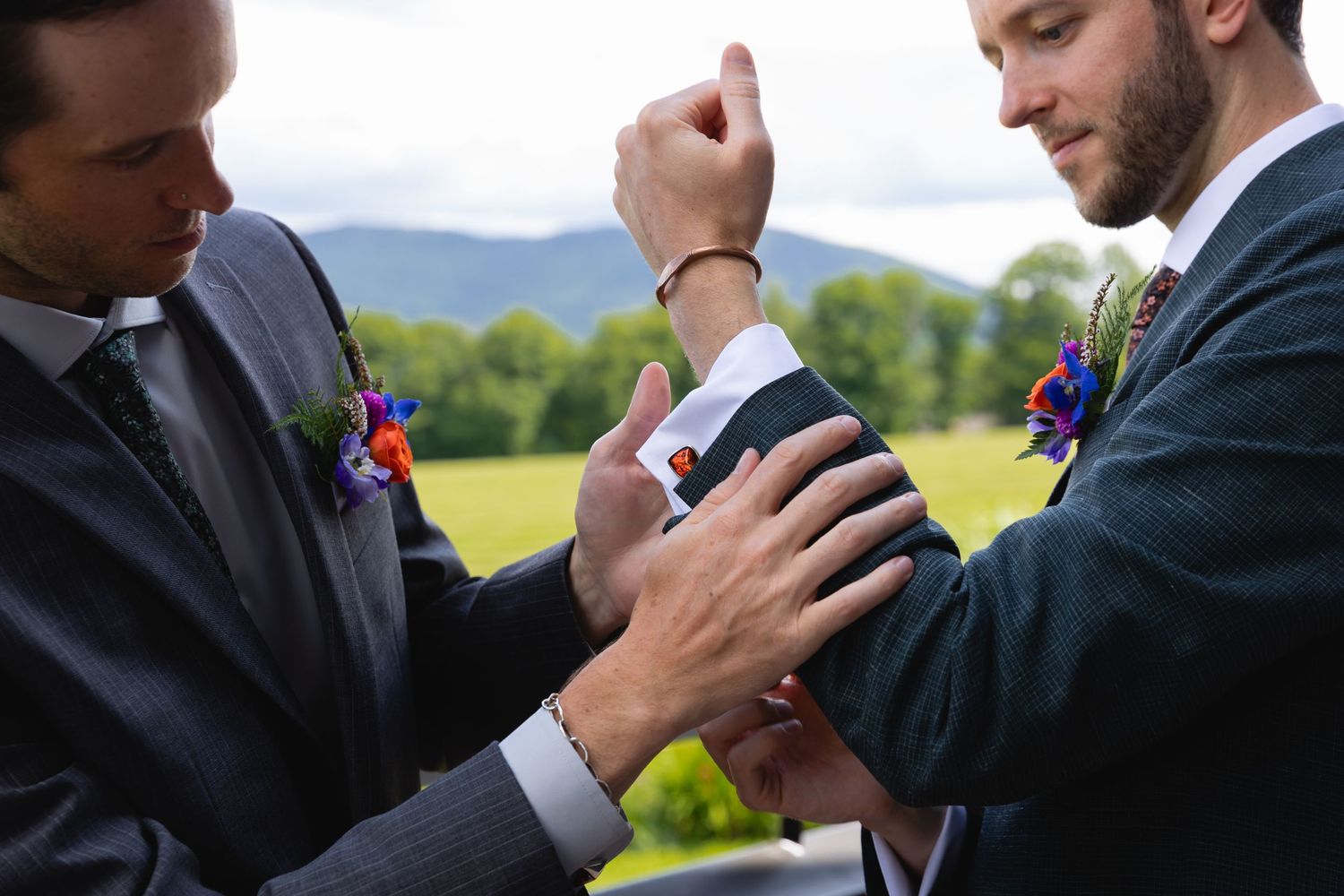 Close up of two men in suits adjusting formal attire outdoors.