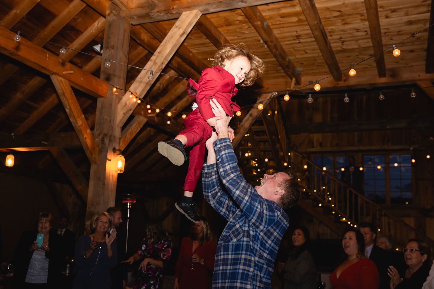 A playful celebration moment captured in a rustic wooden barn with string lights creating a warm ambiance.
