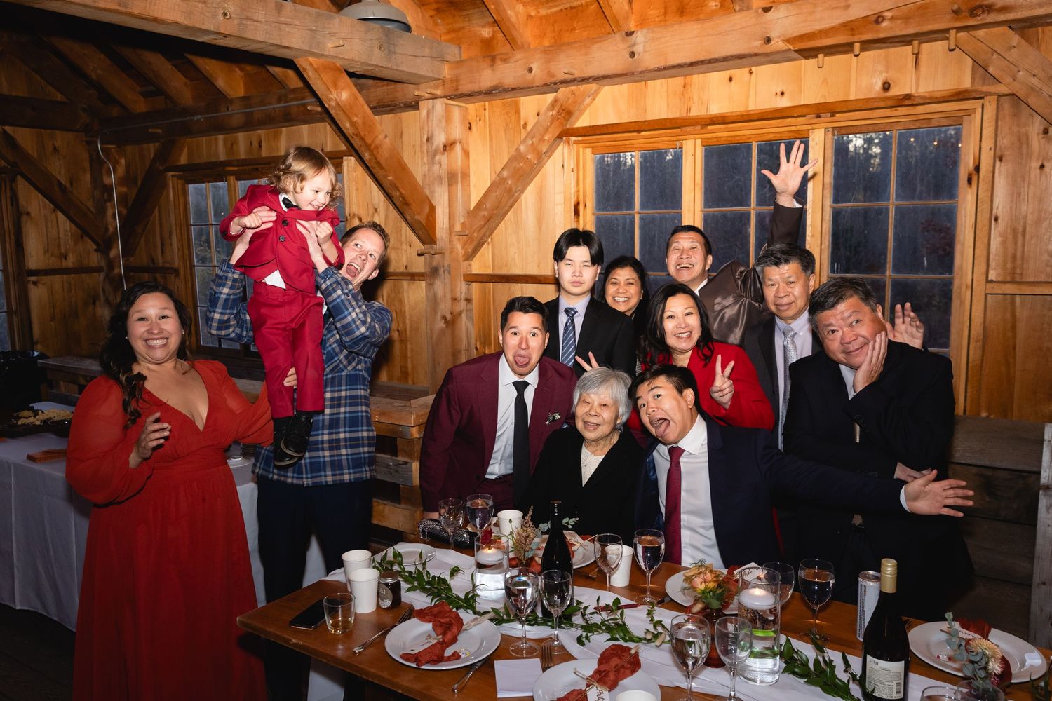 Guests celebrate at a festive holiday dinner gathering inside a rustic wooden barn venue with decorated tables.