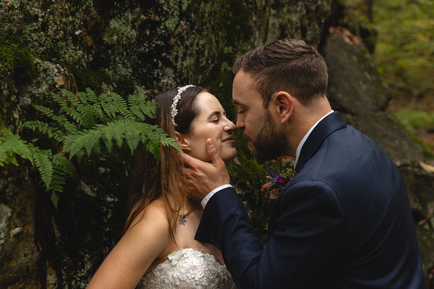 An intimate wedding portrait captured against lush green ferns and forest backdrop.