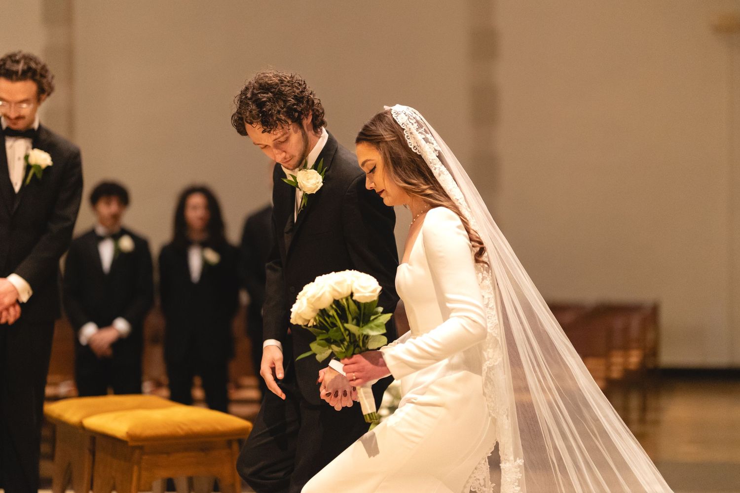A wedding ceremony taking place in a church with a bride in white dress and veil holding a bouquet of flowers.