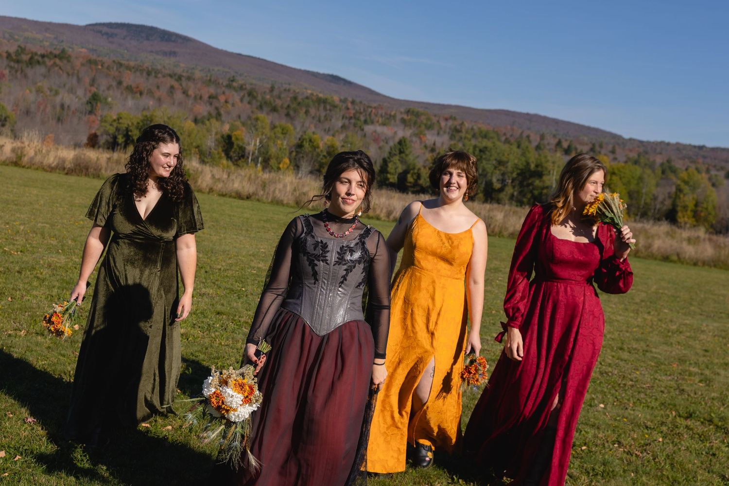 Wedding group walking together across a green meadow with mountain views on a bright fall afternoon.