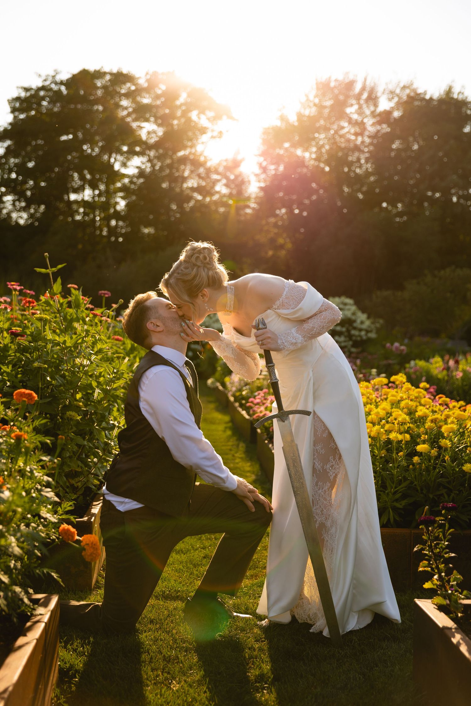 A couple shares a tender moment in a flower garden during golden hour with sunlight creating a magical glow.
