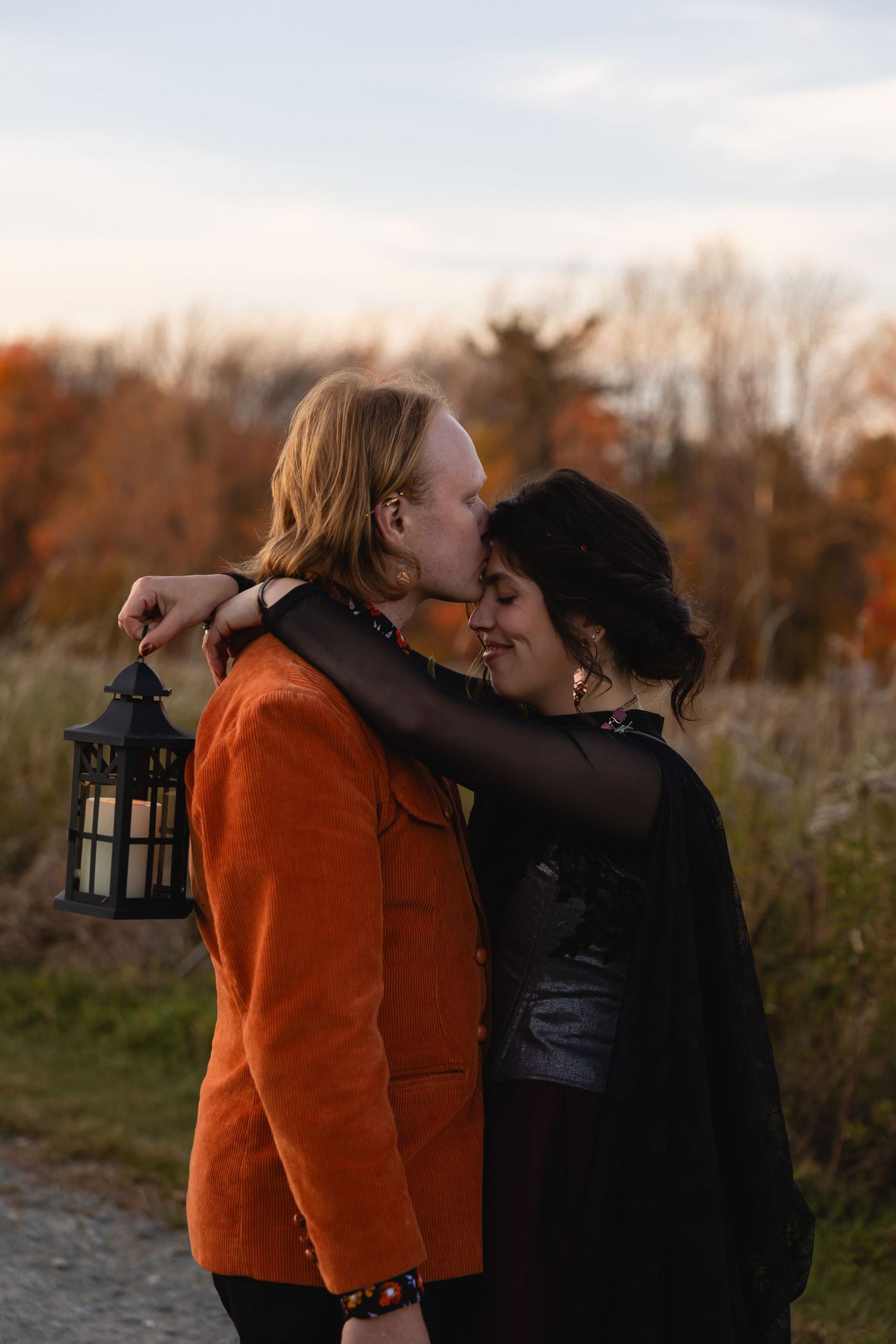 A couple shares a romantic moment at sunset while holding a vintage lantern in an autumn field.