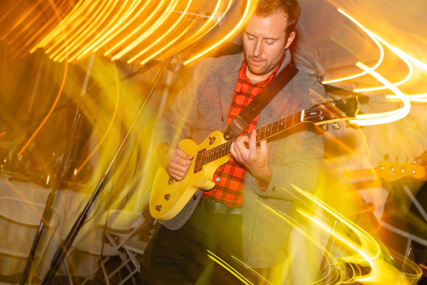 Long exposure concert photography shows streaks of golden light trails against dark background during live performance.