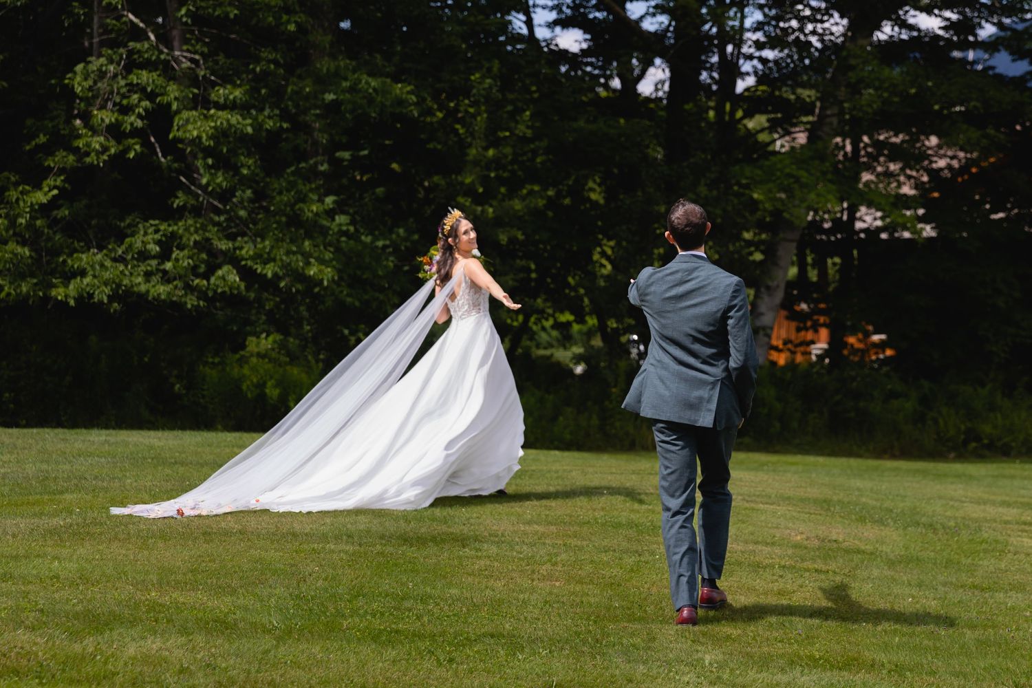 A photographer captures a bride twirling in her flowing white dress on a sunlit lawn.