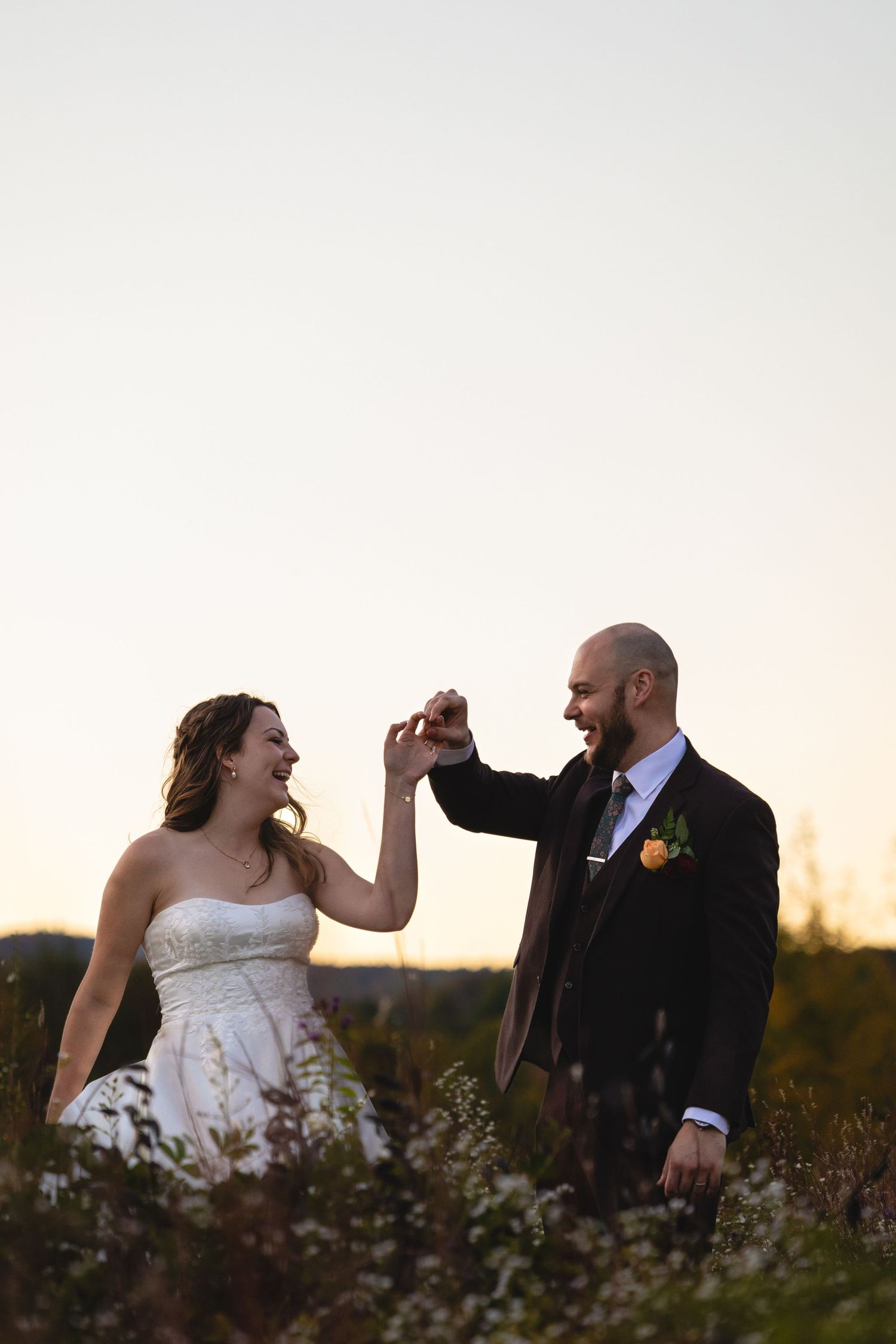 A couple shares a joyful moment together in a field at sunset during their wedding celebration.