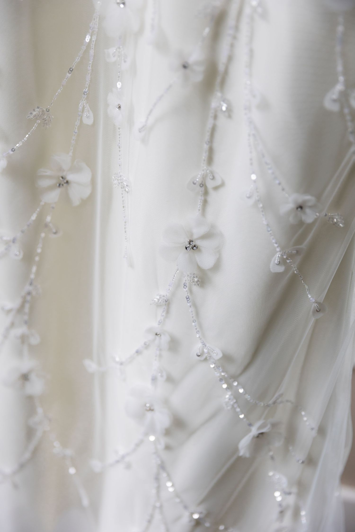 Delicate white beaded details and embroidery on flowing wedding dress fabric create an ethereal texture.