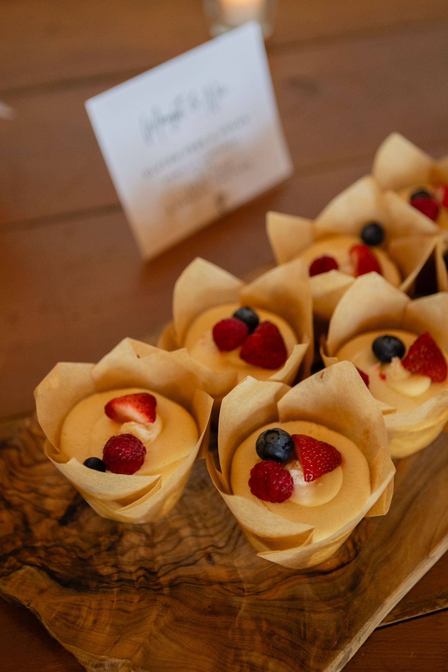 Mini dessert cups filled with cream and topped with fresh berries arranged on a wooden board.
