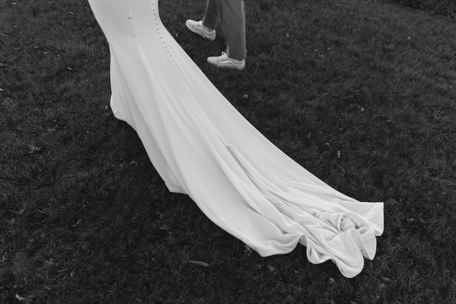 Close-up detail of a white wedding dress train flowing on grass.