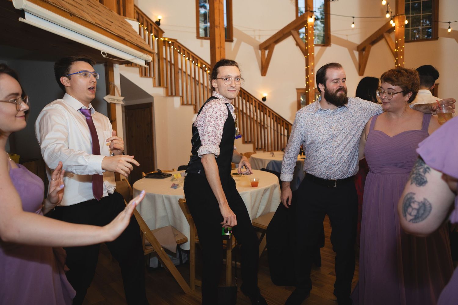 Wedding party members dancing and socializing in formal attire at an indoor reception.