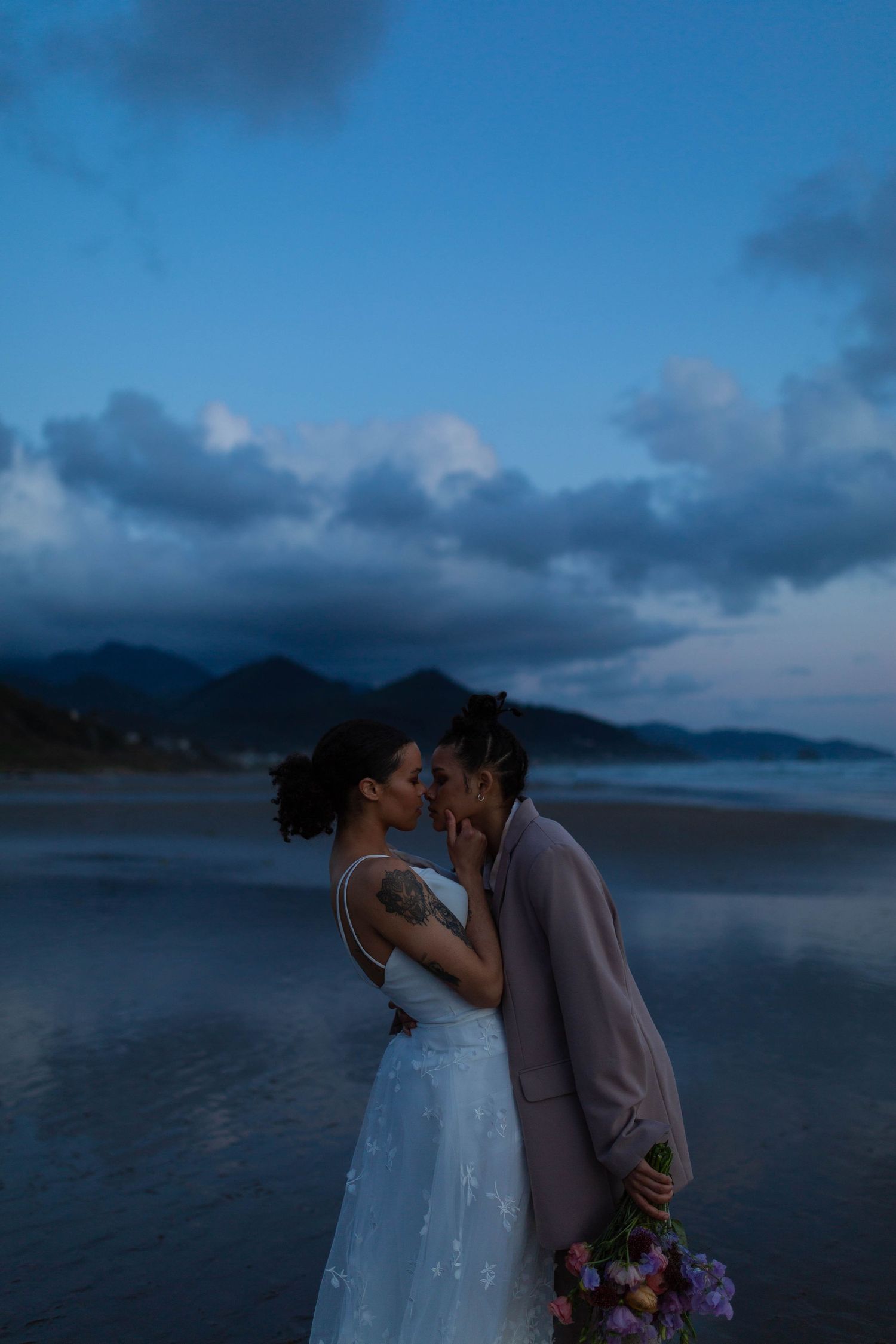 A couple shares a tender moment on a misty beach at twilight.