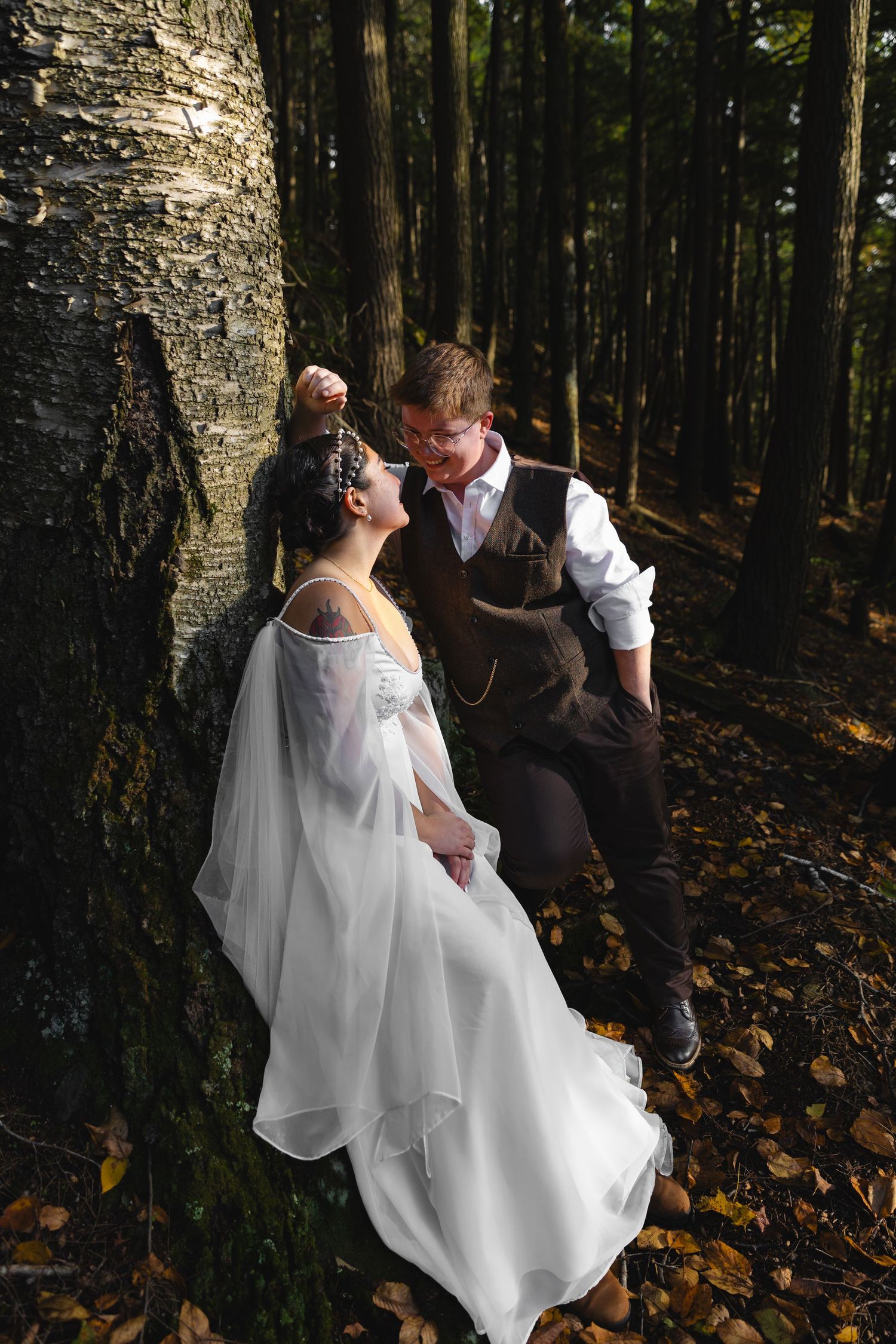 A romantic moment between newlyweds against a large tree trunk in a forest setting.