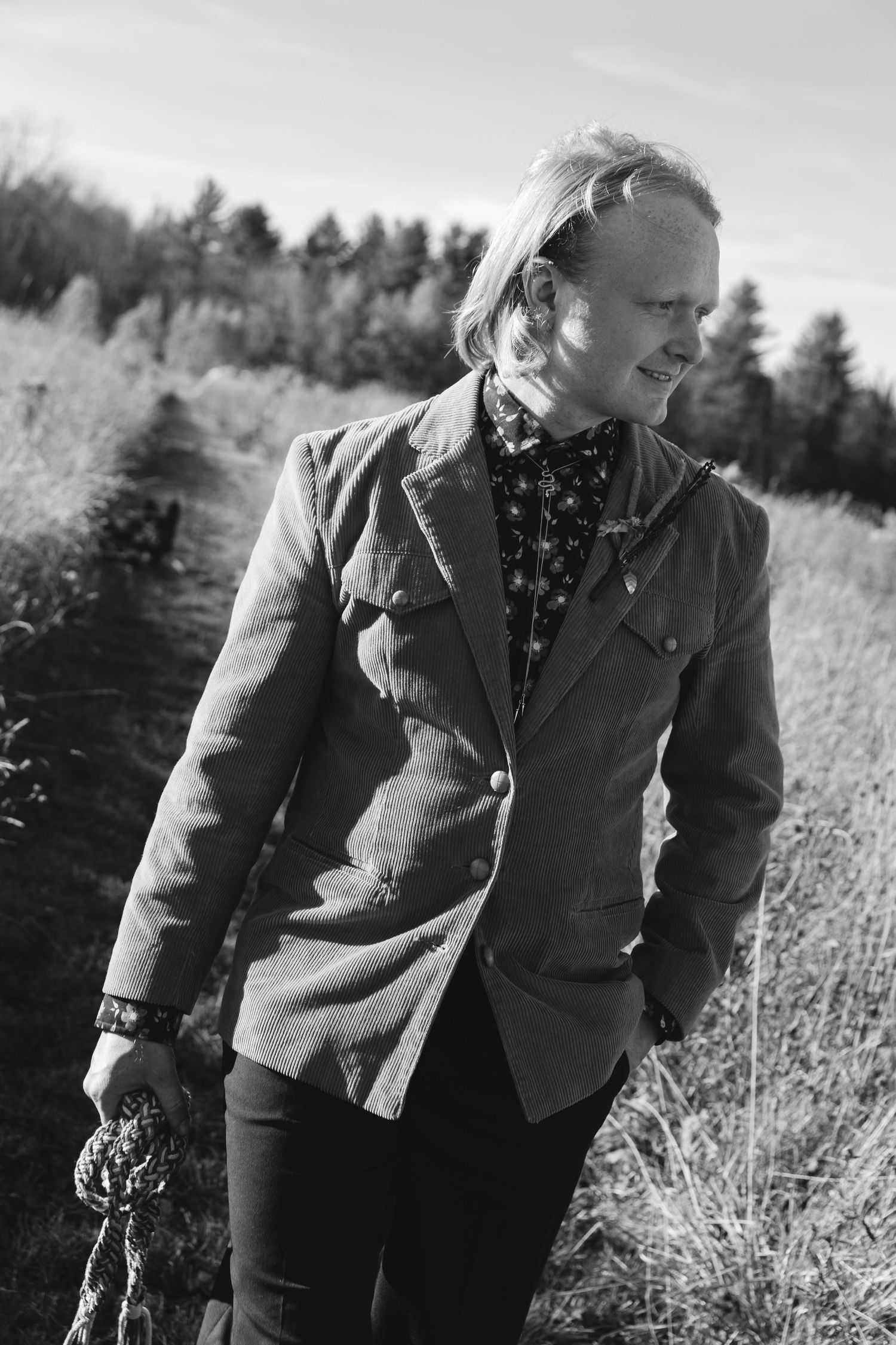 A person in a tweed jacket walks through a sunlit field of tall grasses and wildflowers on an autumn day.