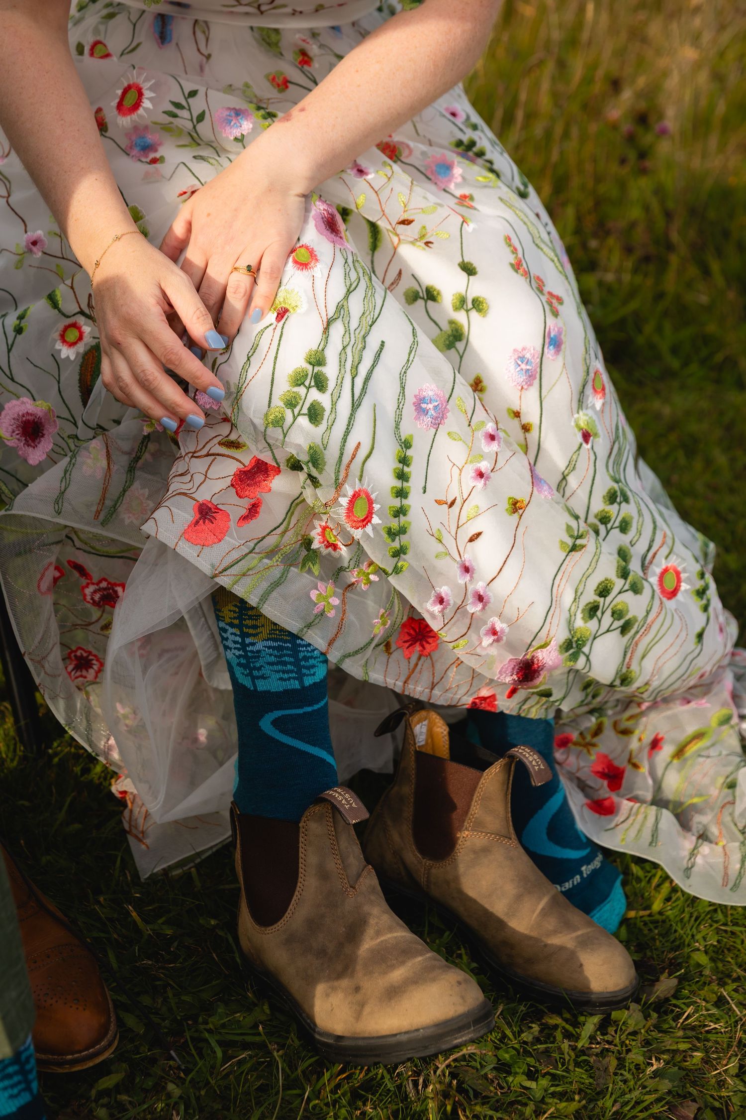 Floral embroidered white dress hem paired with brown leather cowboy boots on grass.