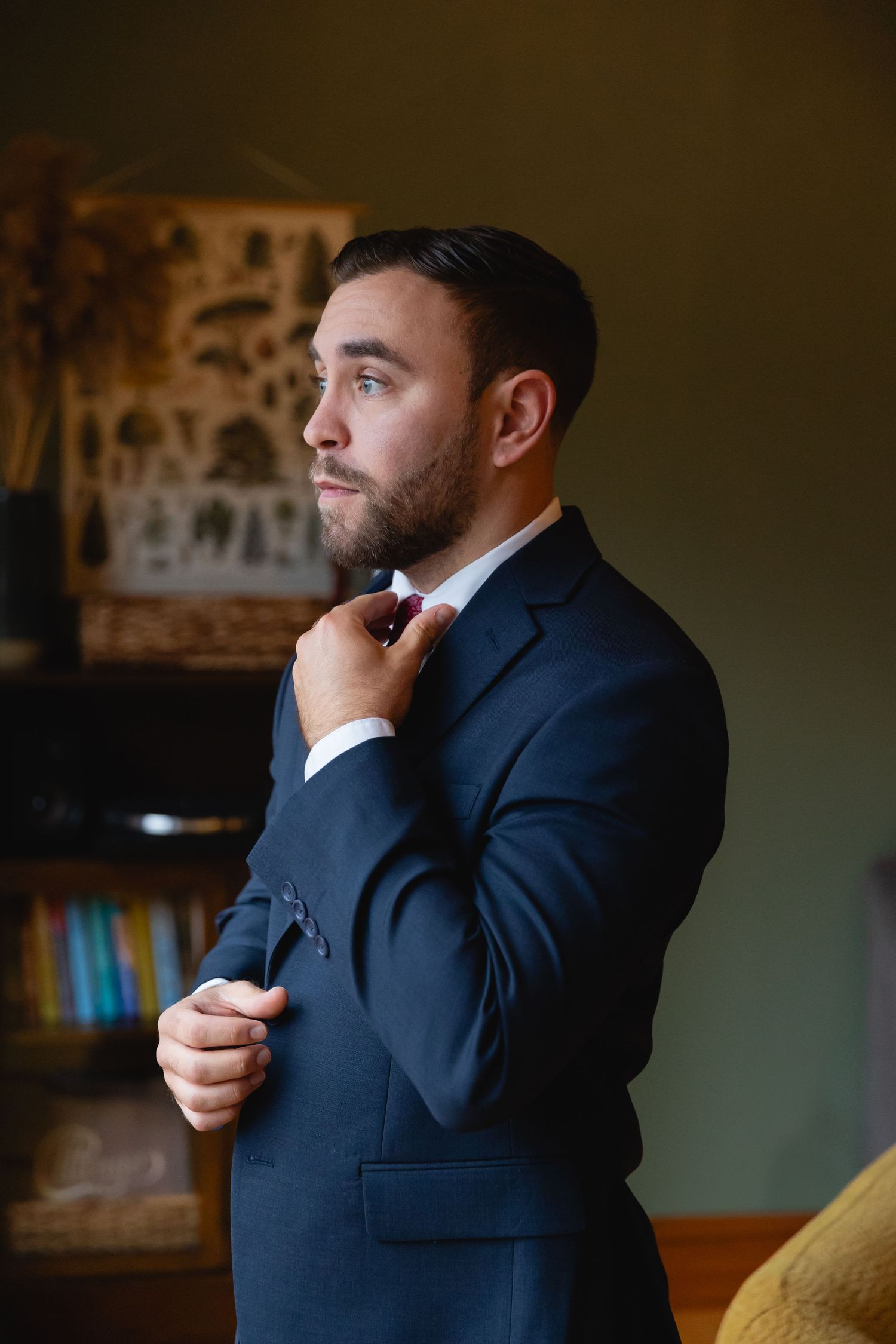 A person in a navy suit adjusts their tie while getting ready indoors.