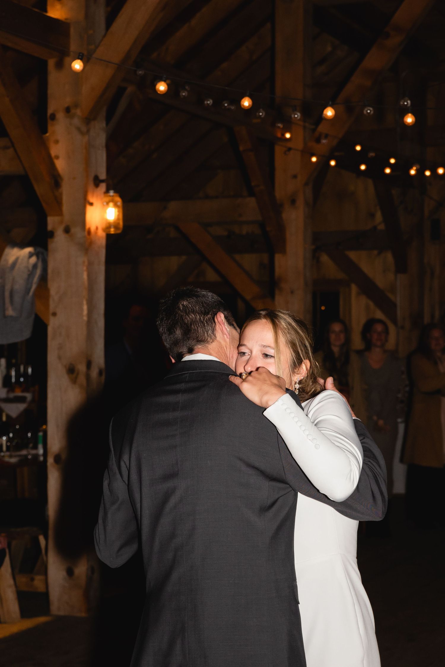 A romantic first dance moment in a rustic barn venue with string lights and wooden beams overhead.