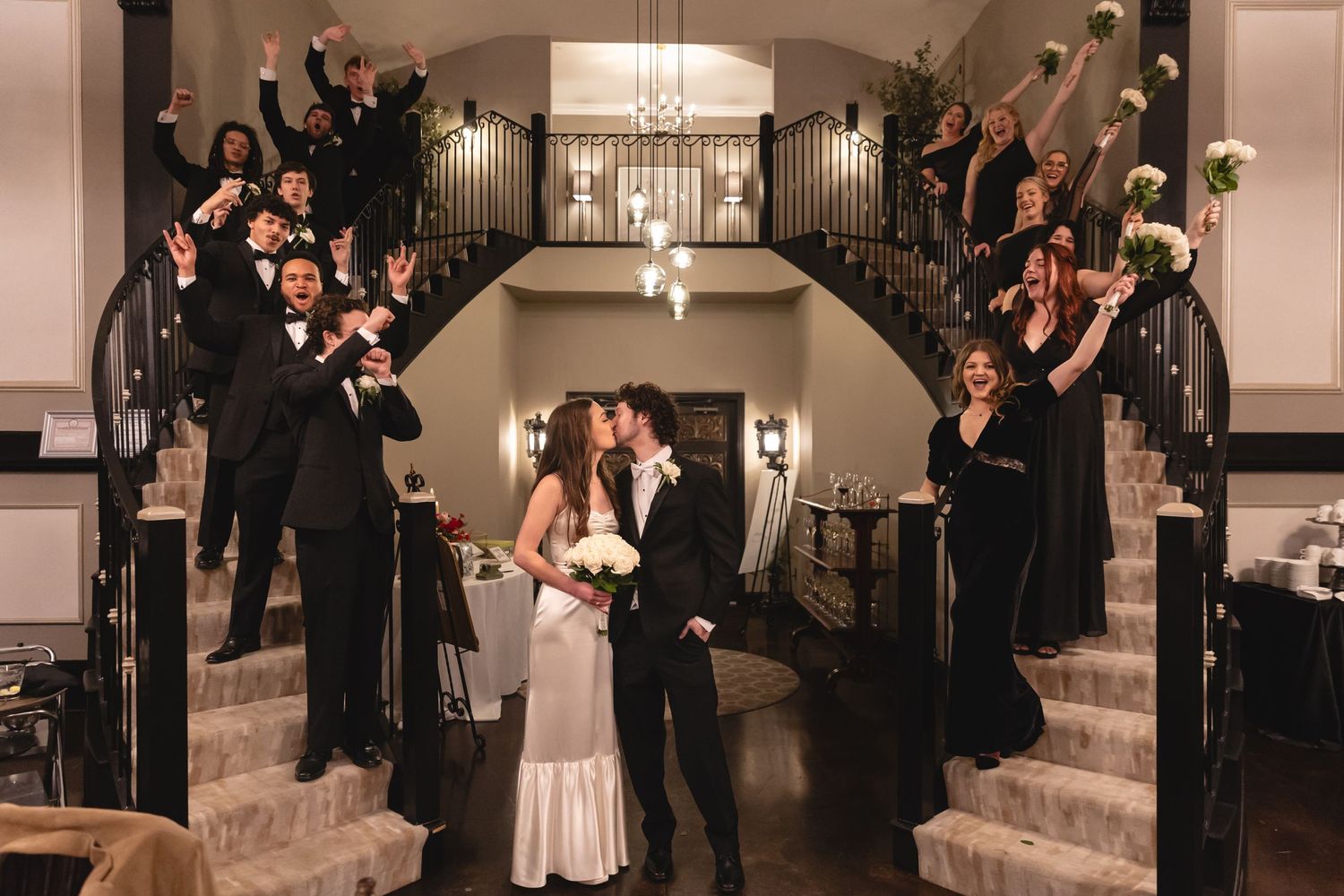 Wedding party gathers on grand staircase in dramatic formation with couple at center during reception celebration.
