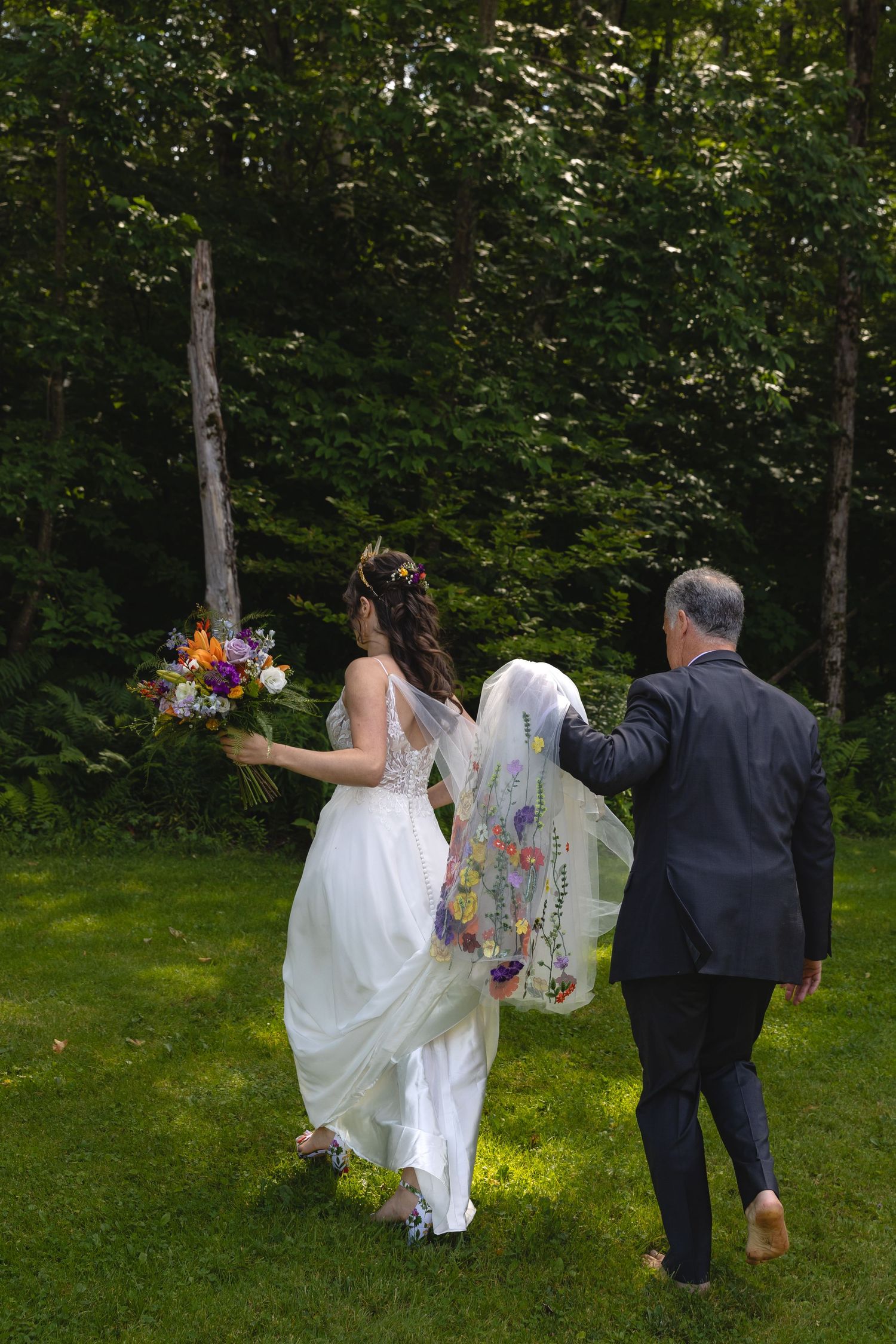 Wedding party walking through a garden path with flowing dress and vibrant bouquet.