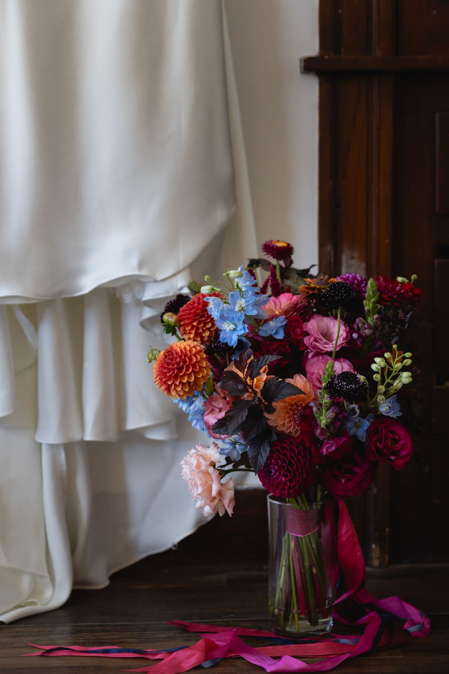 Vibrant floral arrangement with dahlias and mixed flowers in glass vases against a white fabric backdrop.