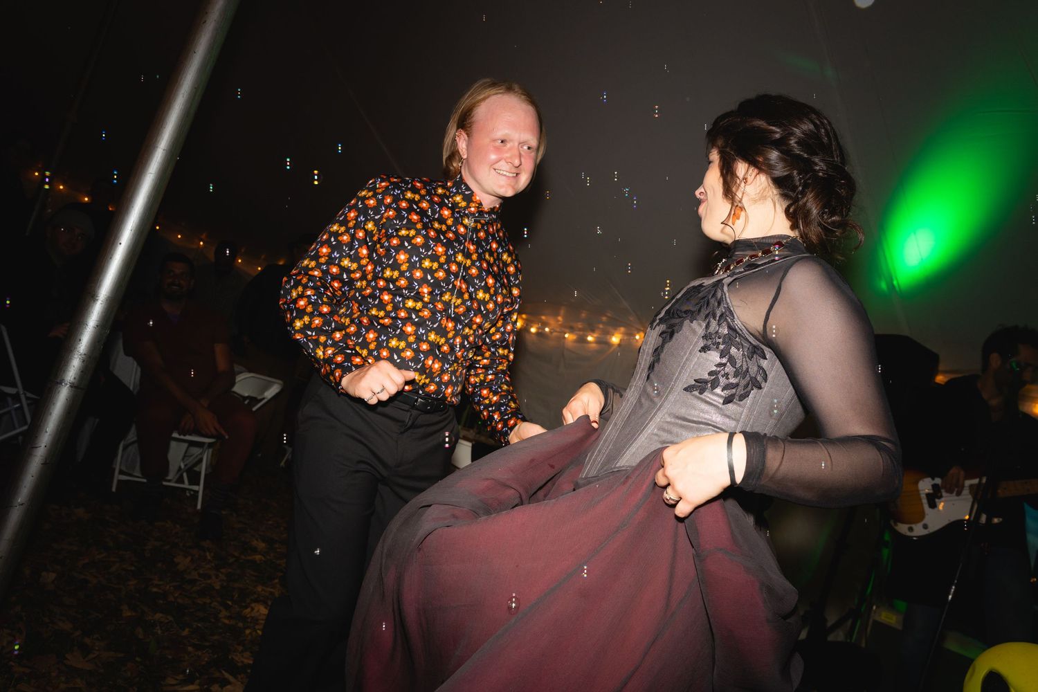 Couples dancing together at a dimly lit party venue with green lighting and string lights in the background.