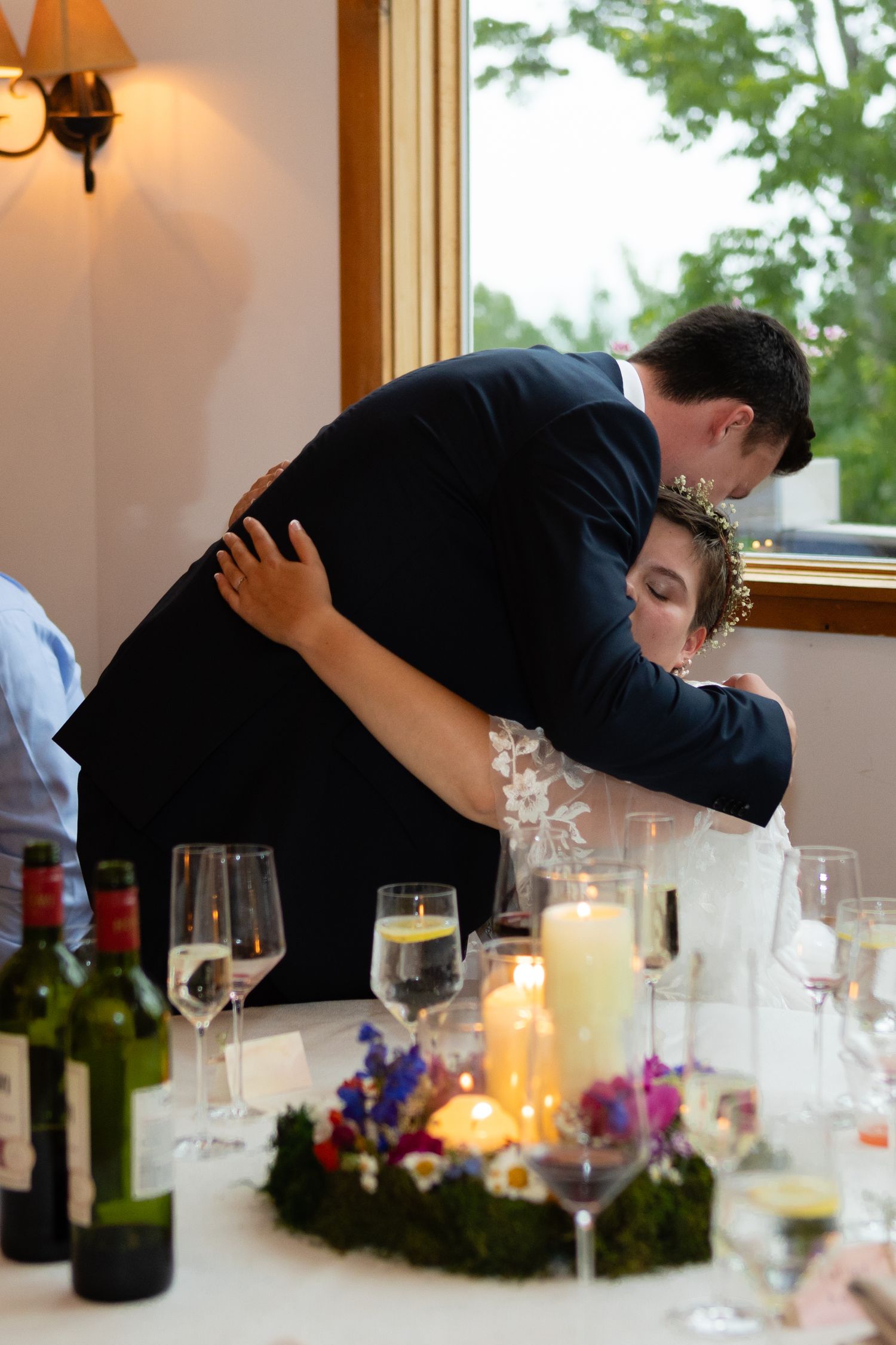 Tender moment shared during wedding reception with decorated dining table in foreground.