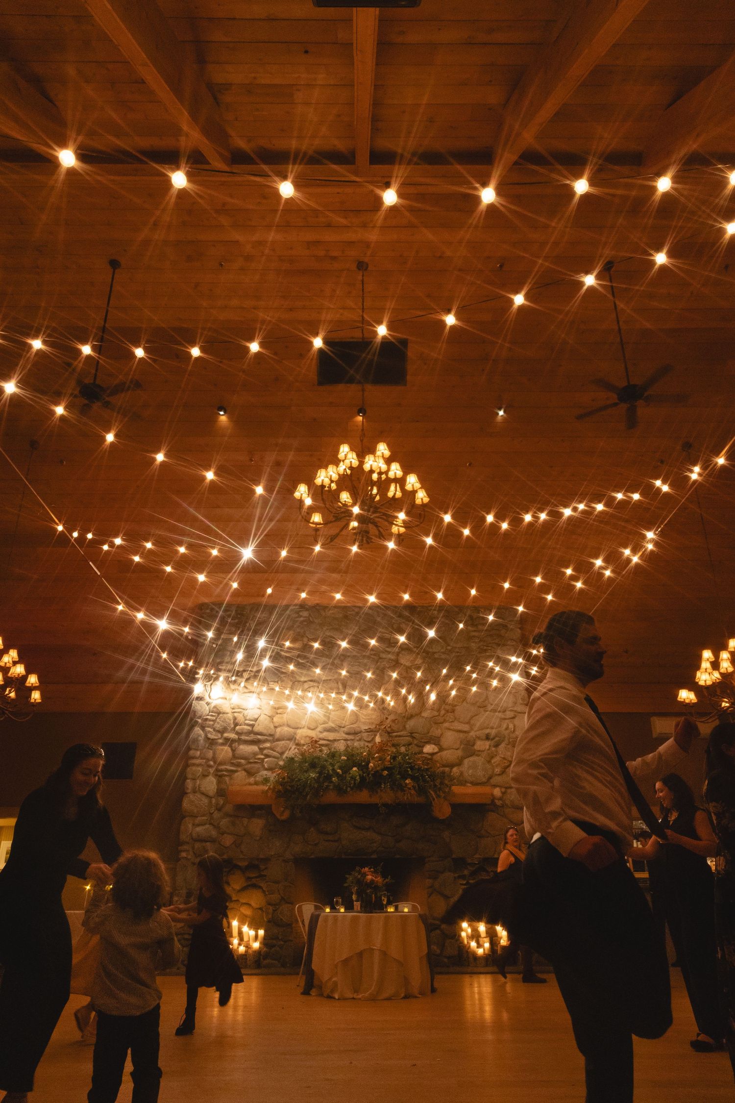 A rustic wedding venue illuminated by romantic string lights and chandeliers.