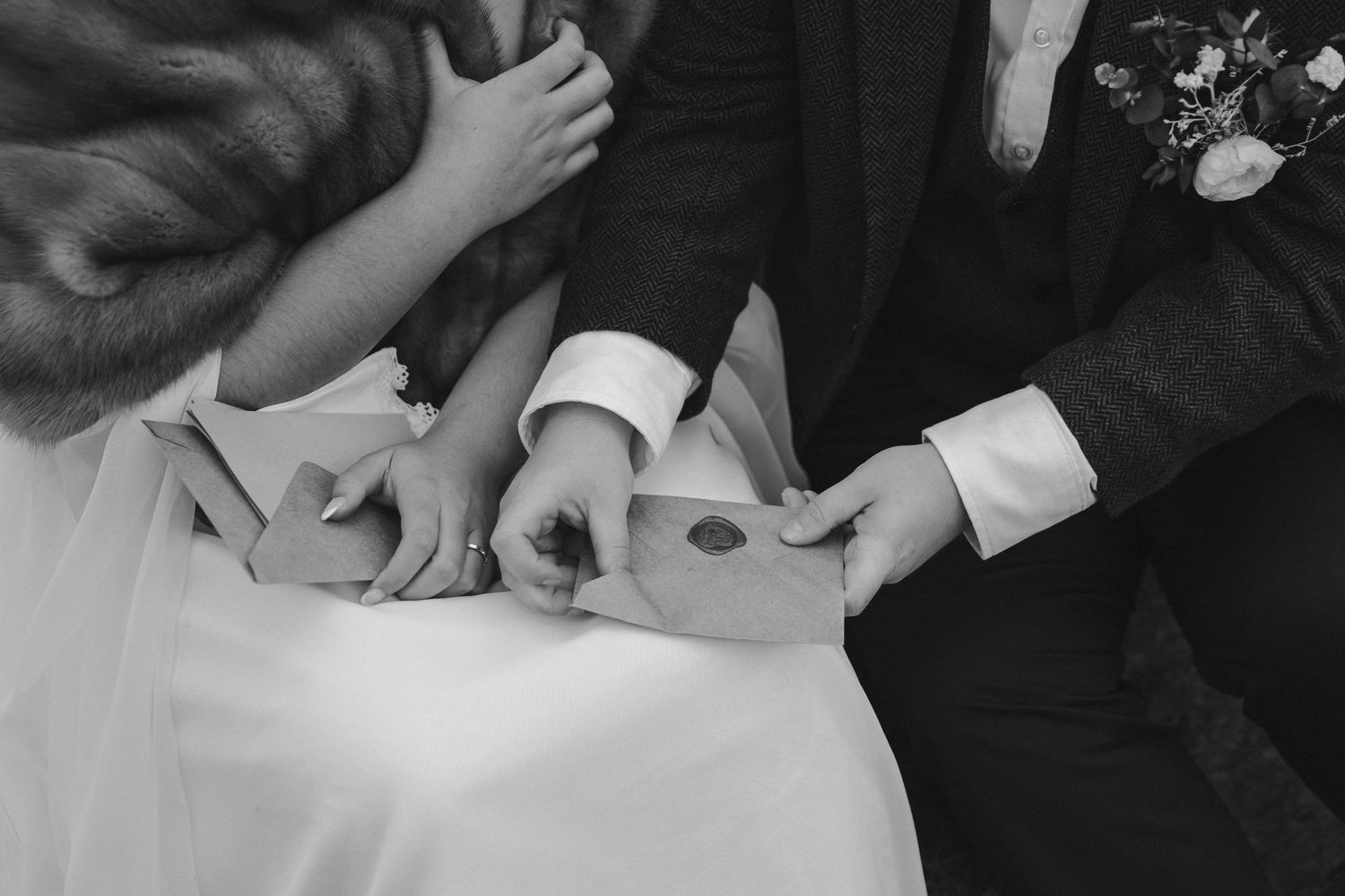 Black and white close-up of hands exchanging rings during wedding ceremony.