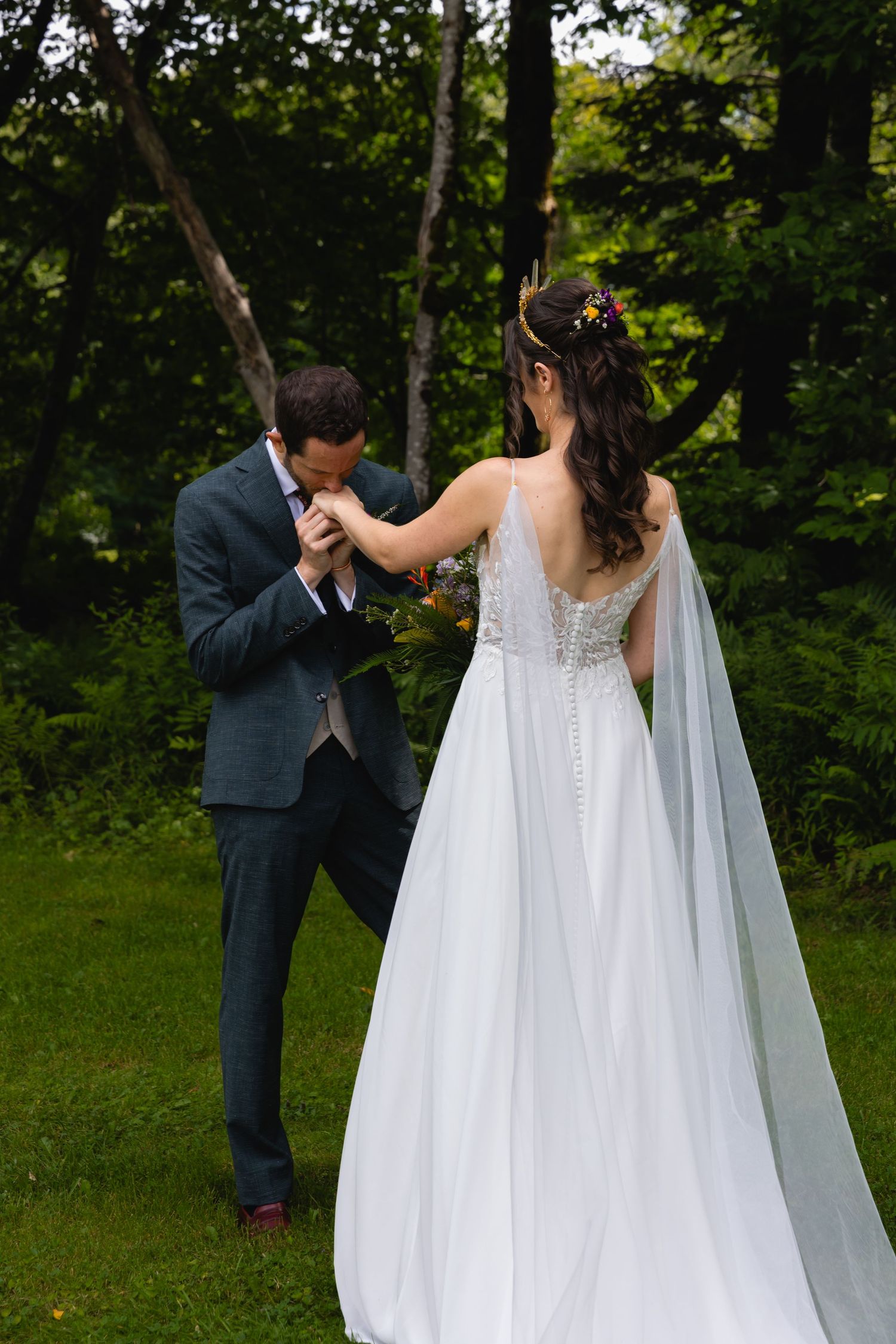 Romantic wedding moment with flowing white dress and veil against forest backdrop.