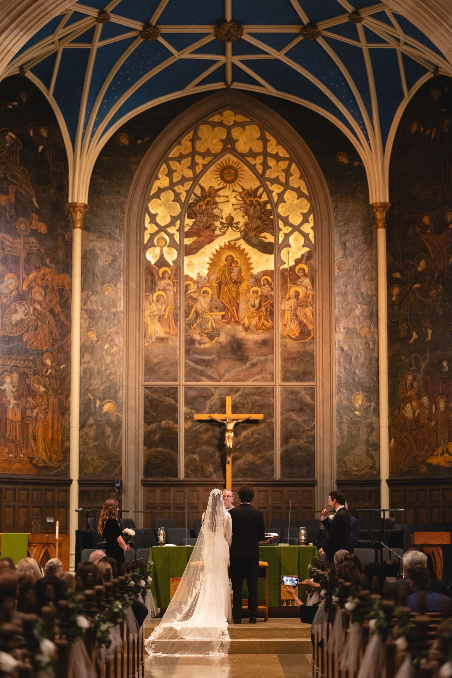 A traditional church wedding ceremony takes place beneath grand Gothic vaulted ceilings with stained glass and religious artwork.