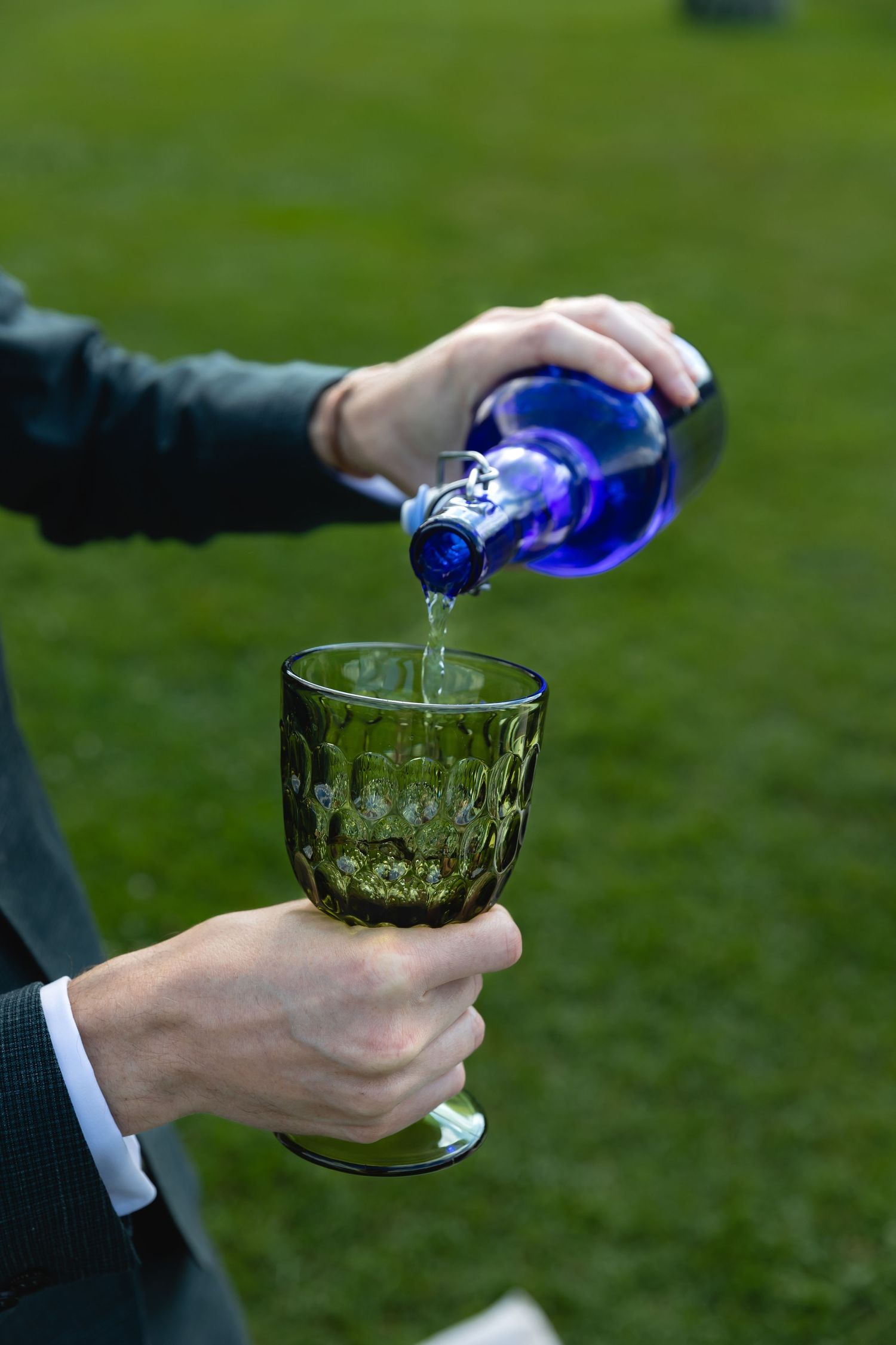Pouring a blue-colored drink into a vintage glass goblet at an outdoor event.