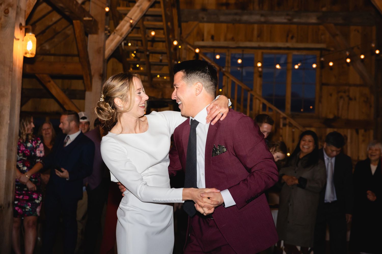 Dancing couple shares a joyful moment in a beautifully lit rustic barn venue.