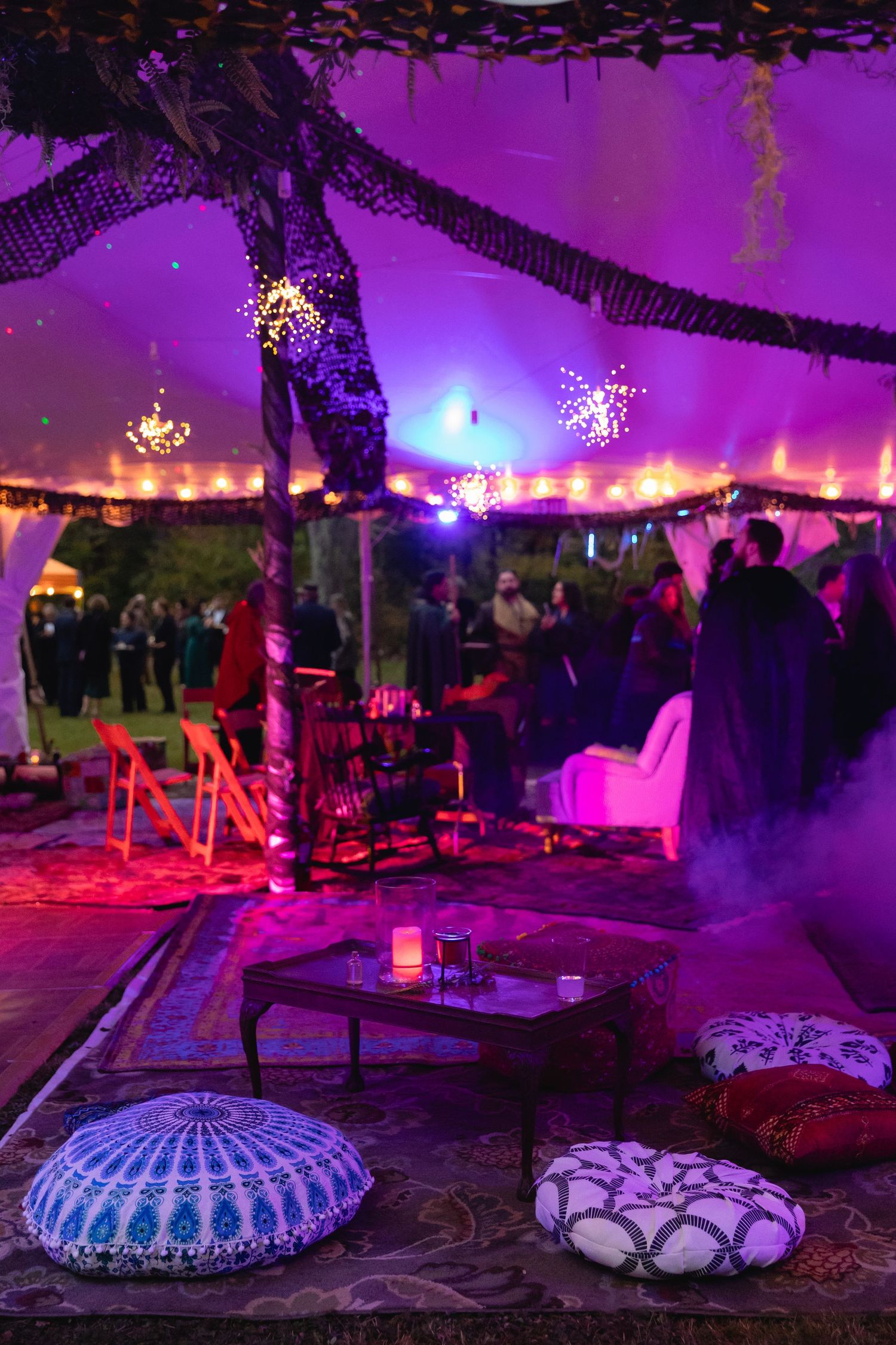Bohemian wedding reception tent with purple lighting, floor cushions, patterned rugs, and festive atmosphere.