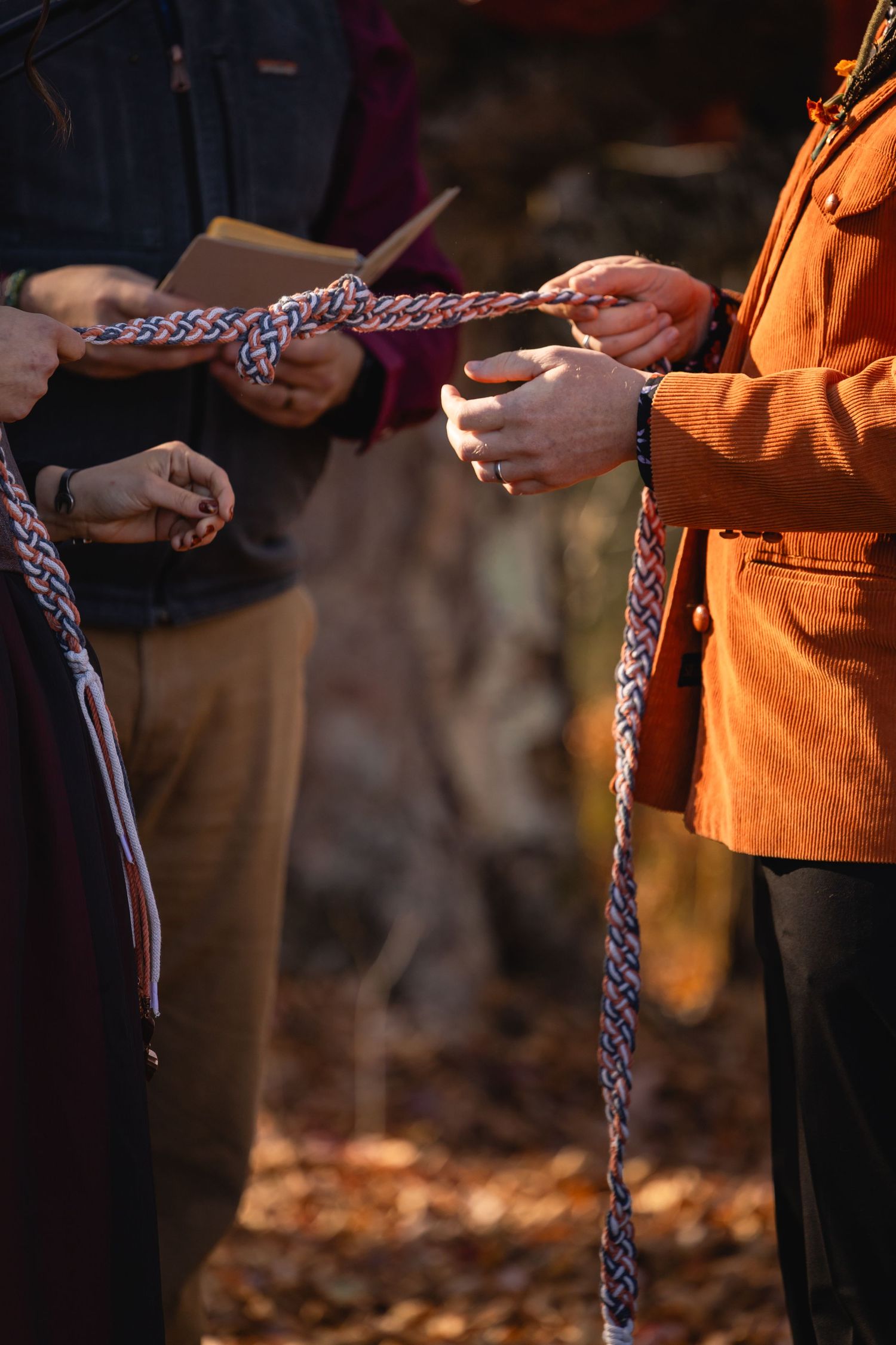 Hands hold a braided rope in warm autumn lighting during an outdoor ceremony.